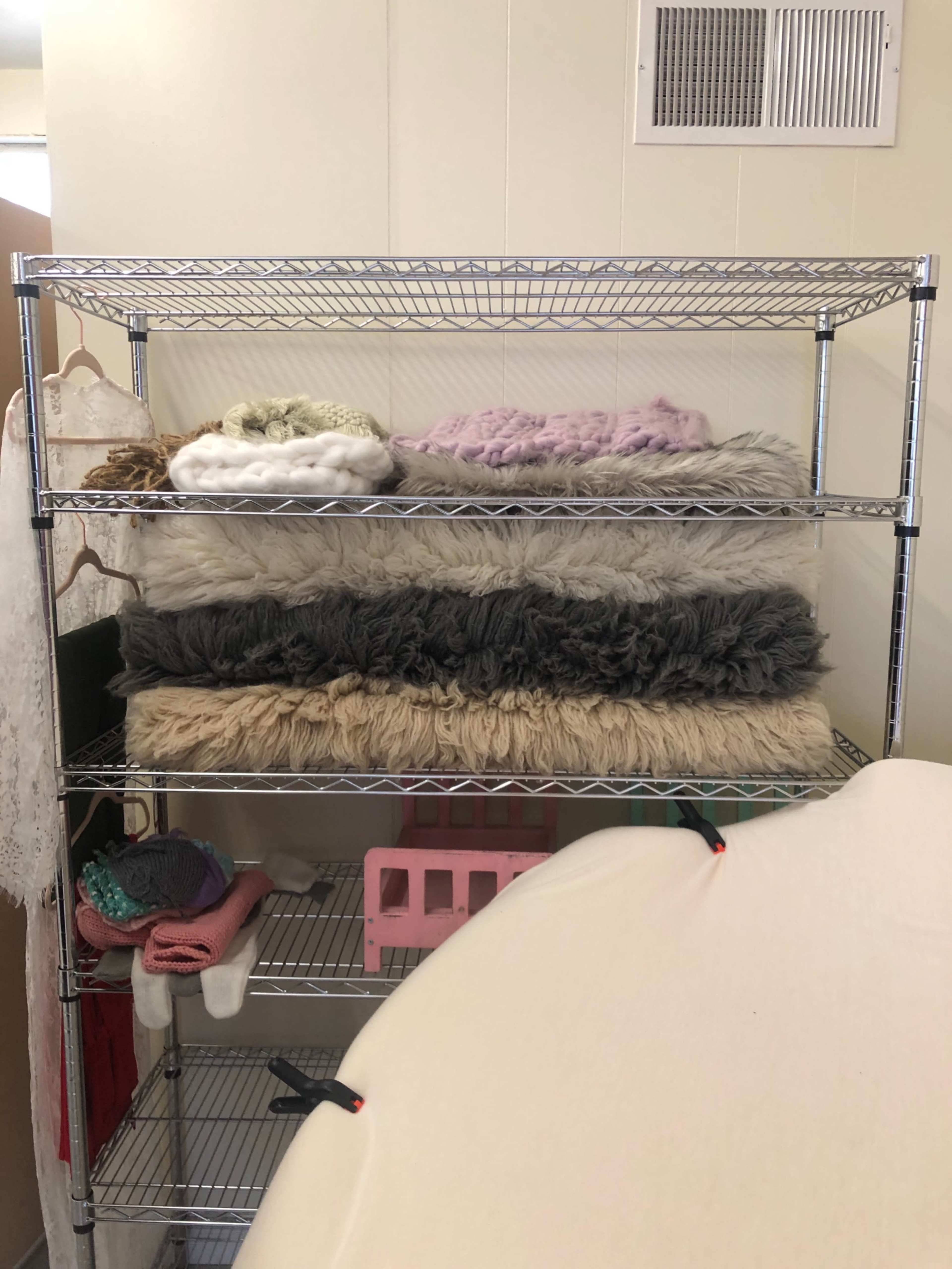 A wire shelving unit holds several stacked blankets and fabric items in a storage room.