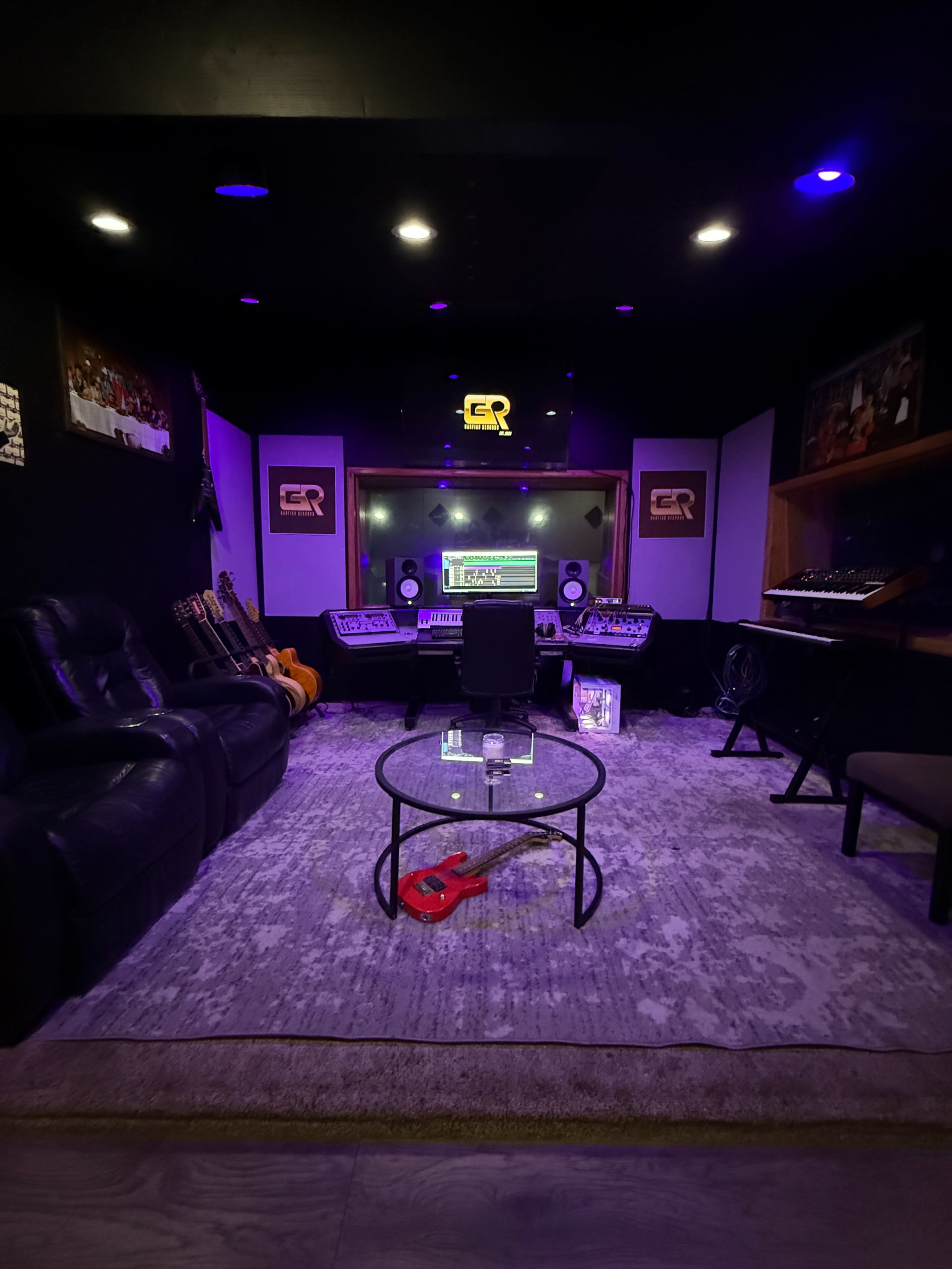 The image shows a music studio with a central mixing desk, surrounding sound equipment, guitars on display, and soft purple lighting.