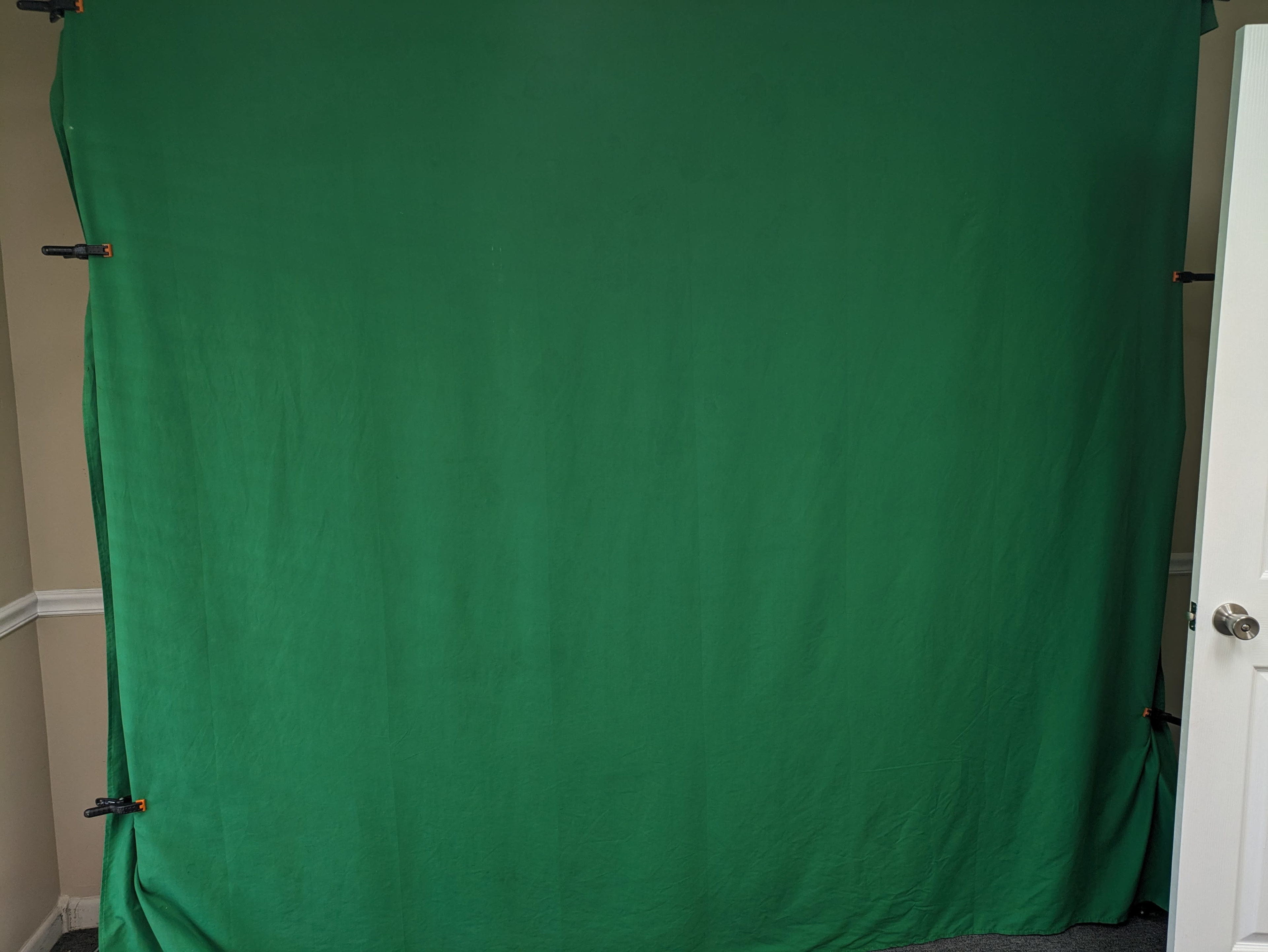 A green fabric backdrop is secured to a wall and is illuminated in a room.