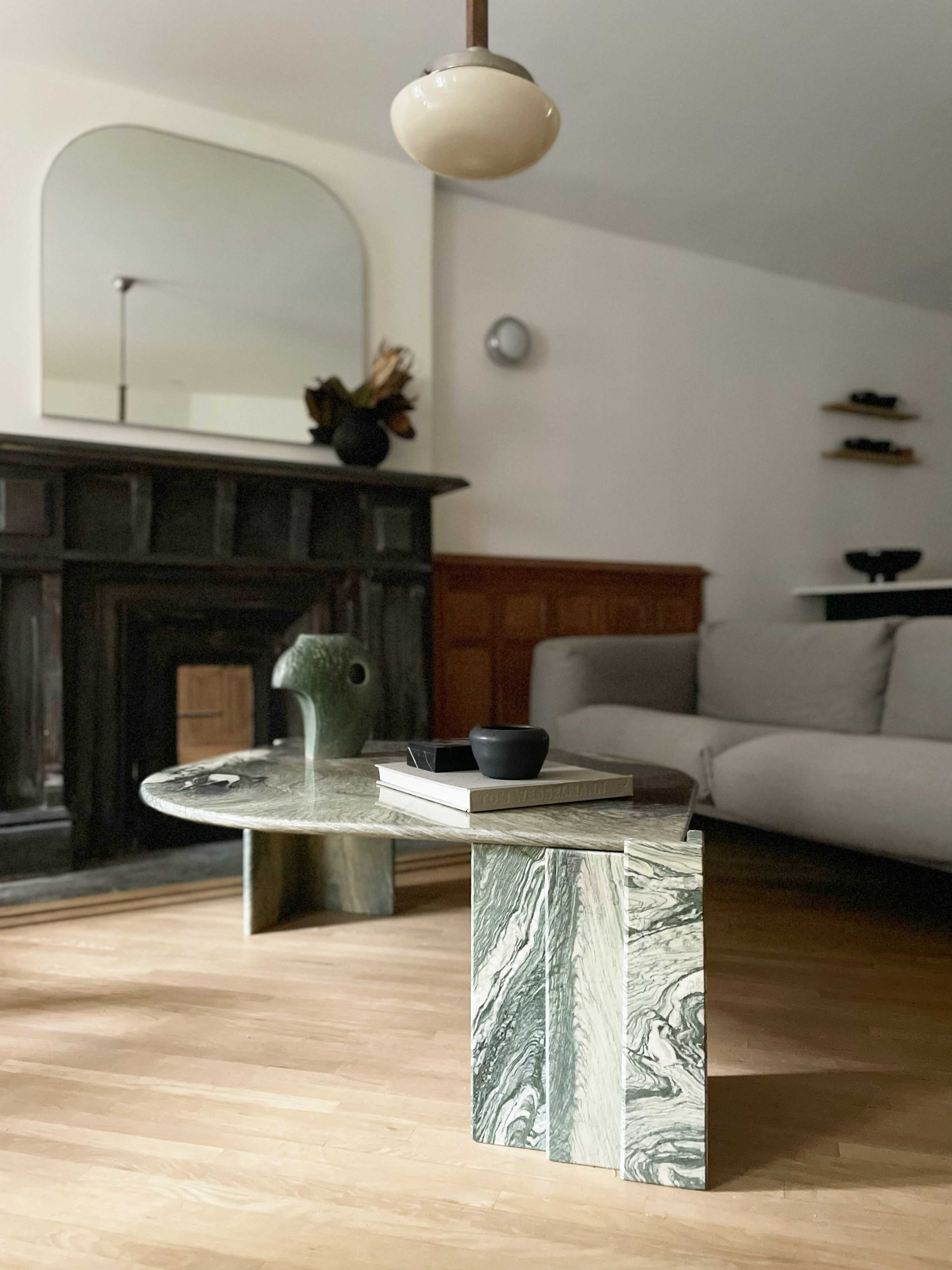 The image features a modern living room with a unique marble coffee table, a beige sofa, and a dark wooden fireplace, complemented by a round pendant light.