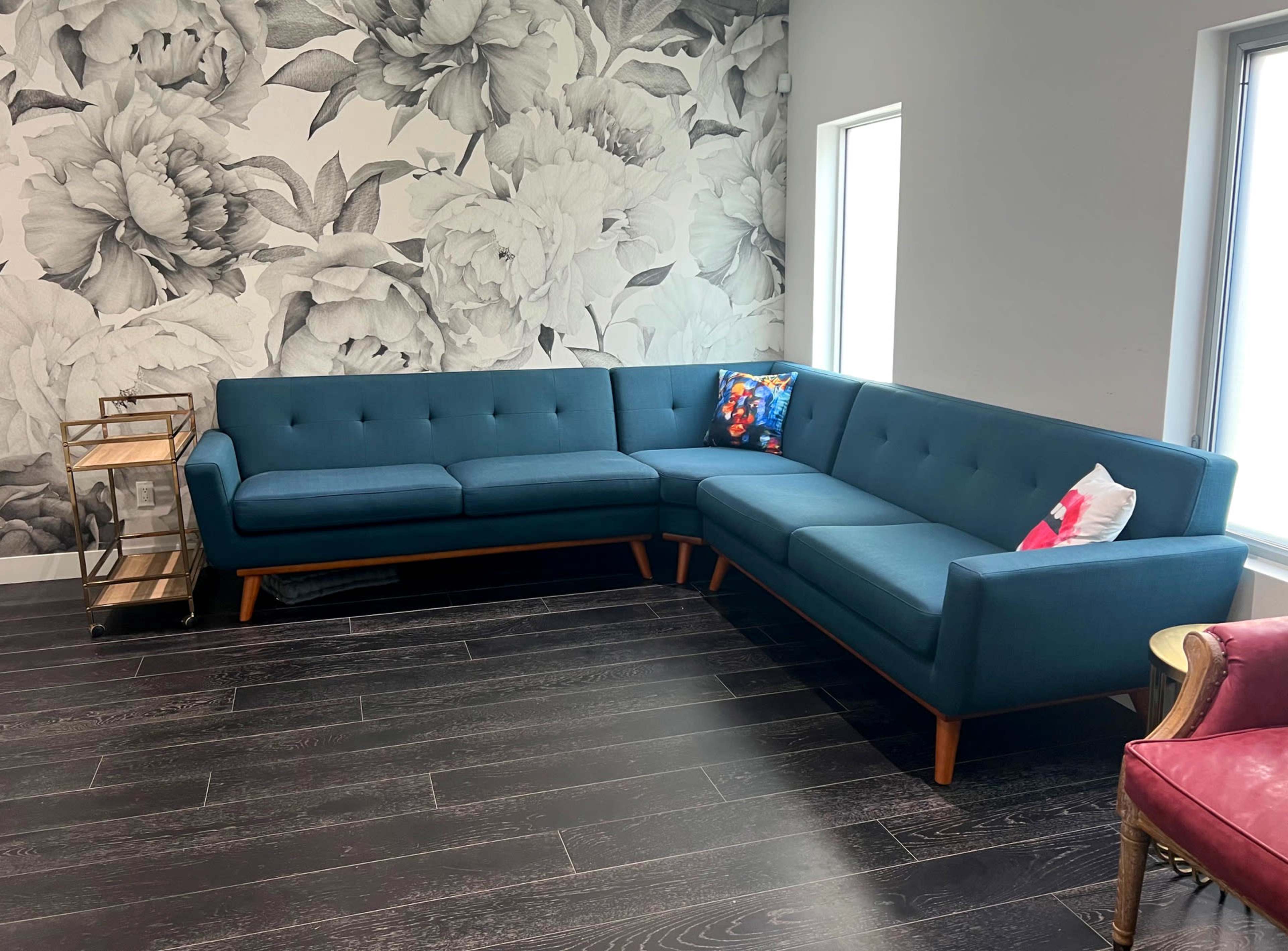 A blue sectional sofa in a modern room with floral wallpaper and wooden flooring.
