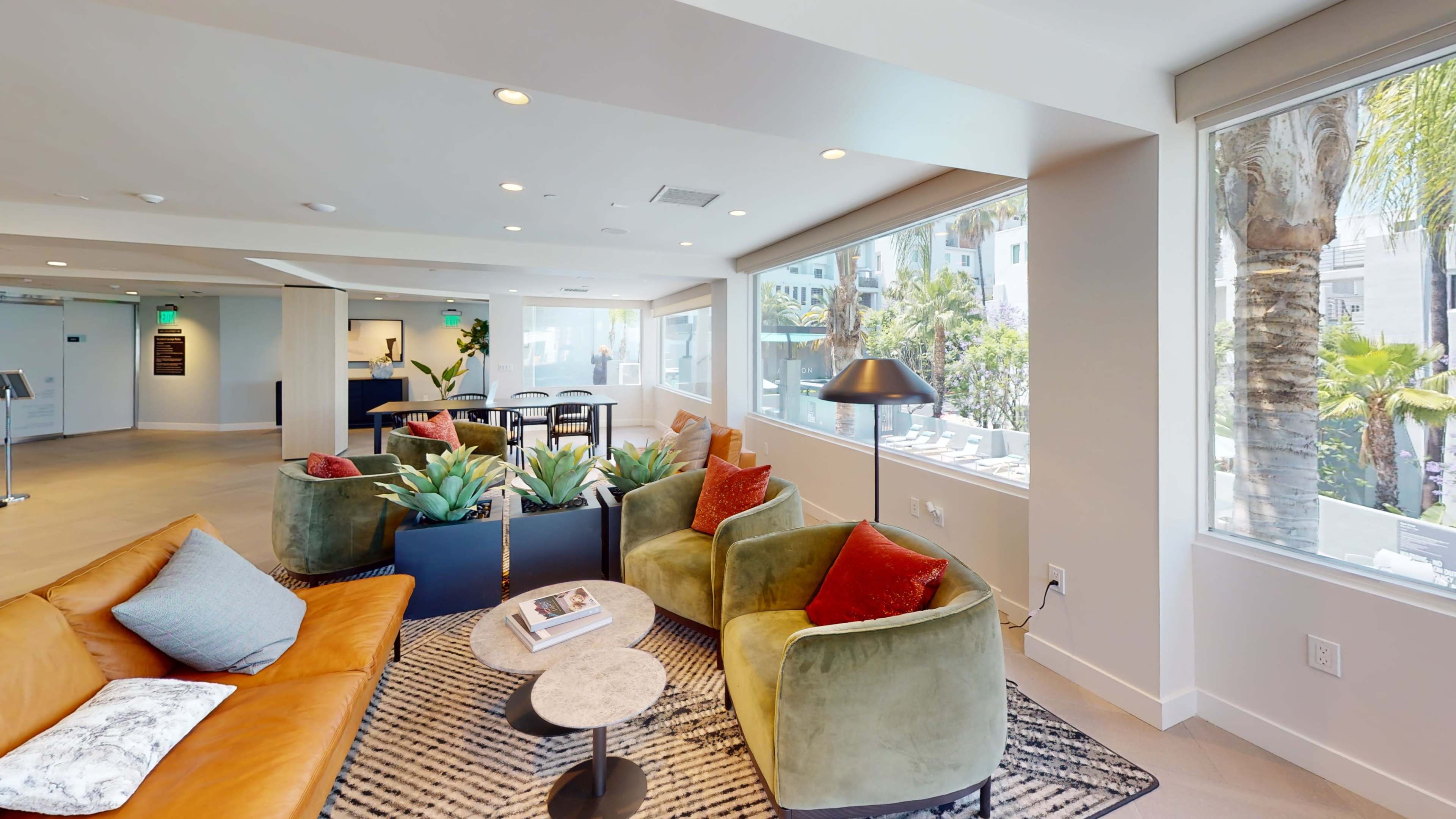 A modern communal lounge area with a mix of colorful seating, potted plants, and large windows allowing natural light.