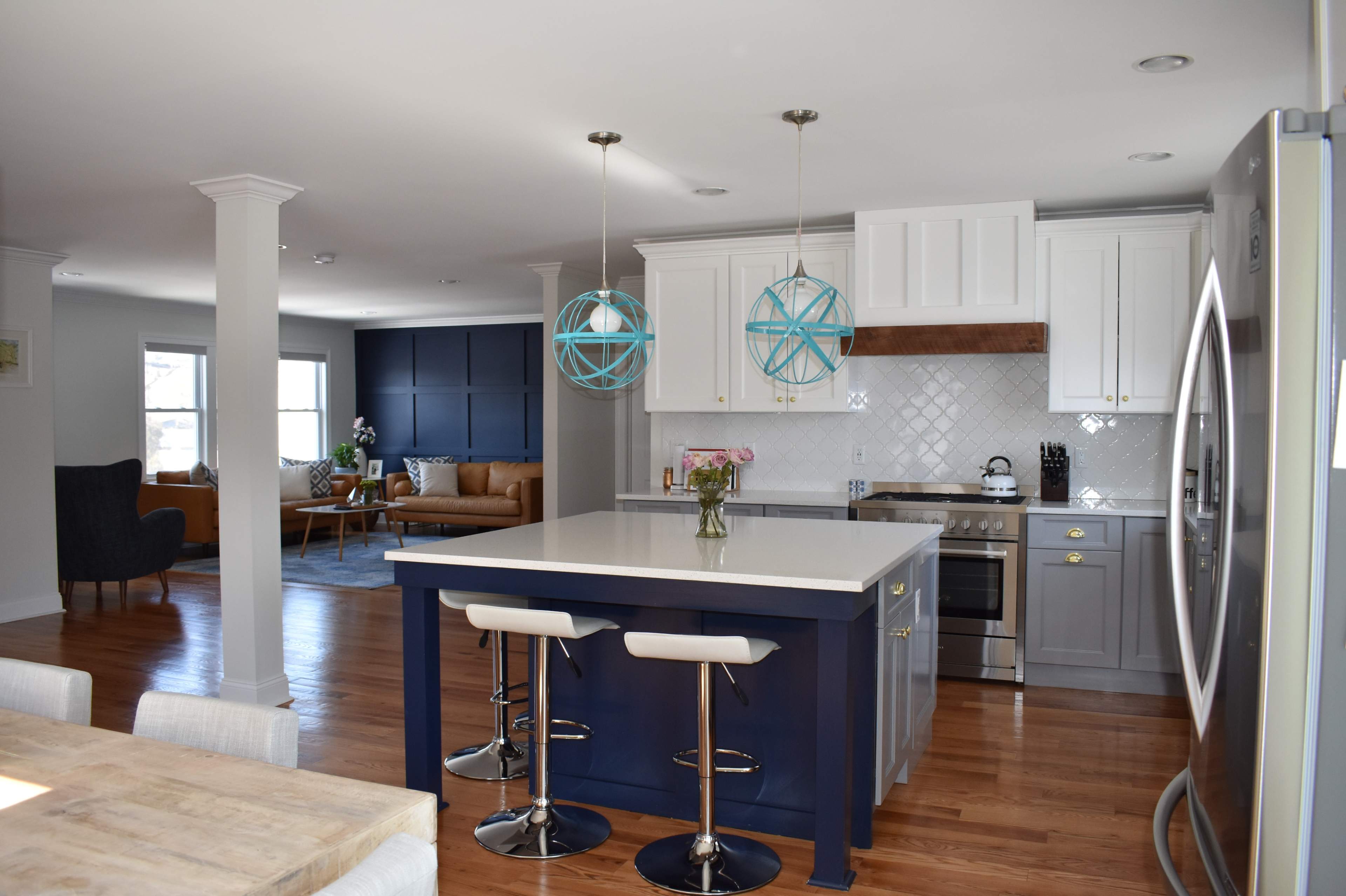 A modern kitchen with a large island, blue pendant lights, and an open layout connecting to a living area furnished with a sofa and chairs.