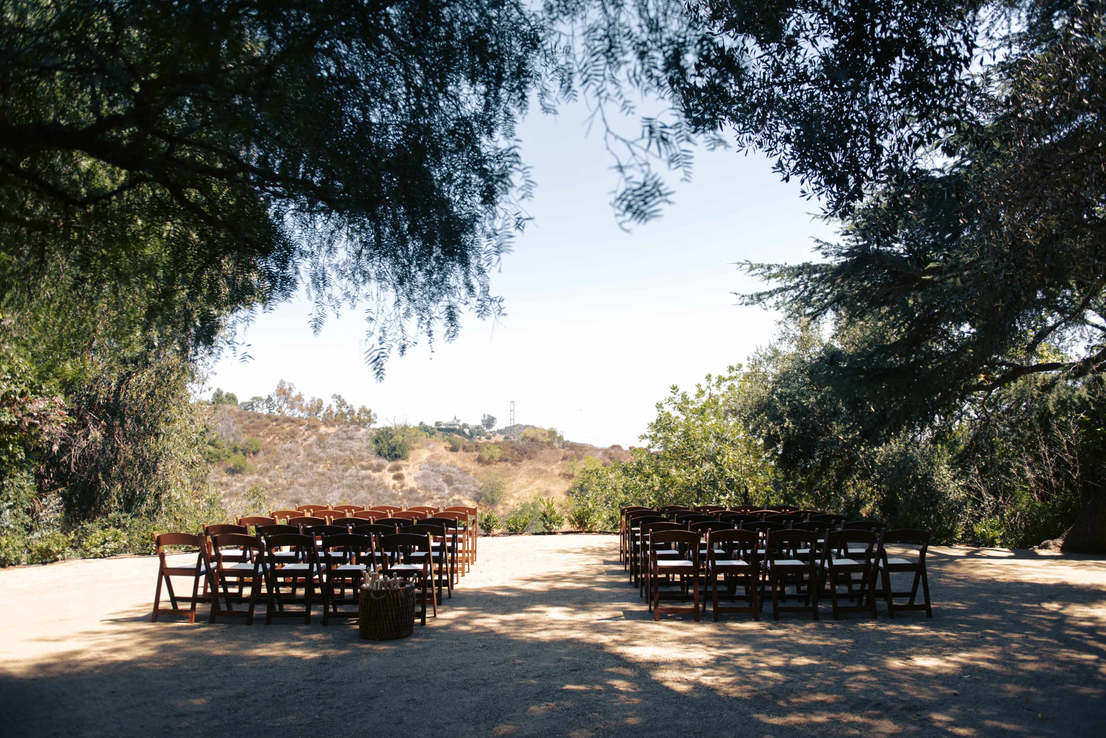 The image shows a cleared outdoor space with two rows of wooden chairs facing a scenic view of a hilly landscape under a clear sky.