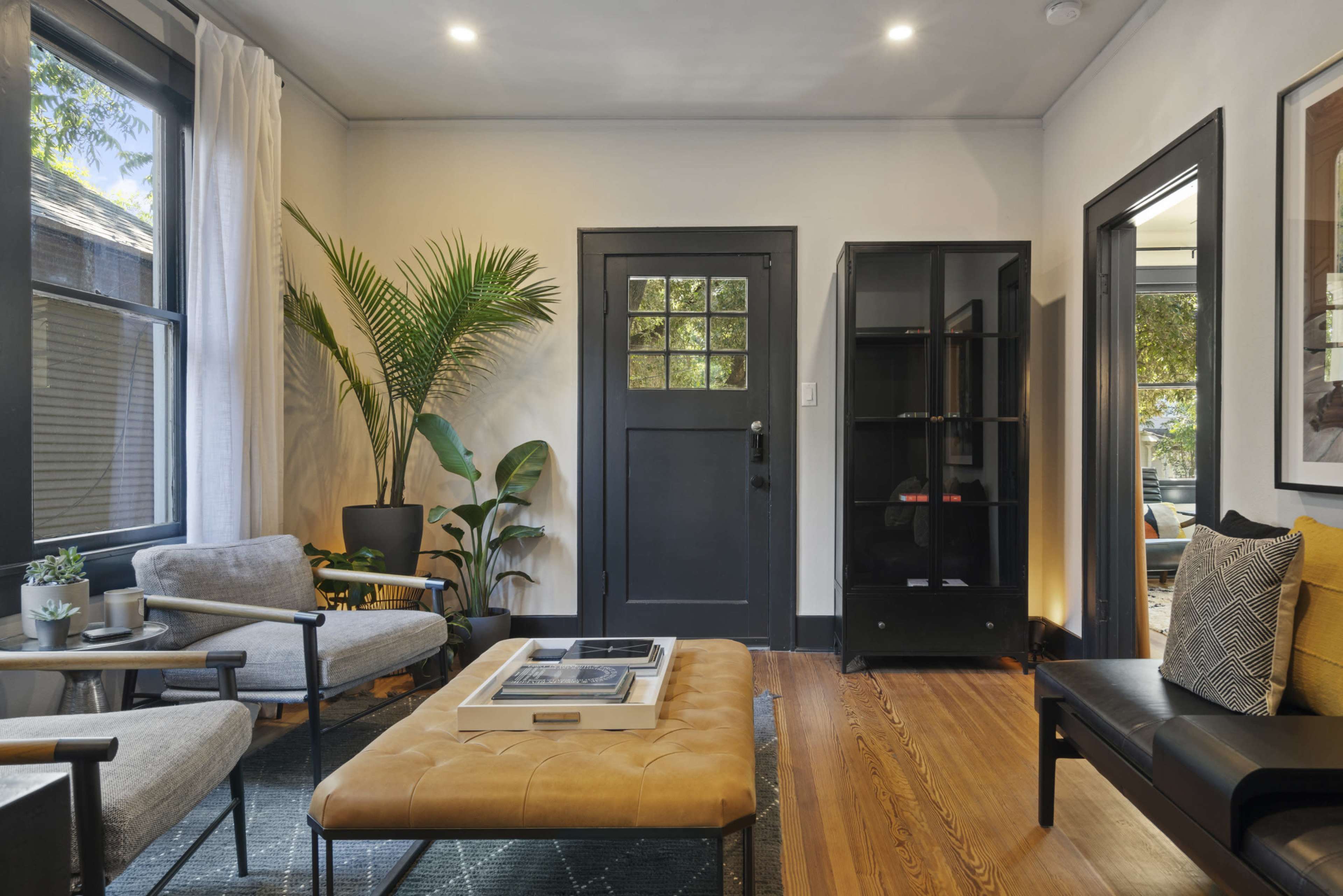 A modern living room with two armchairs, a coffee table, a black door, and a tall bookshelf, complemented by plants and natural light.