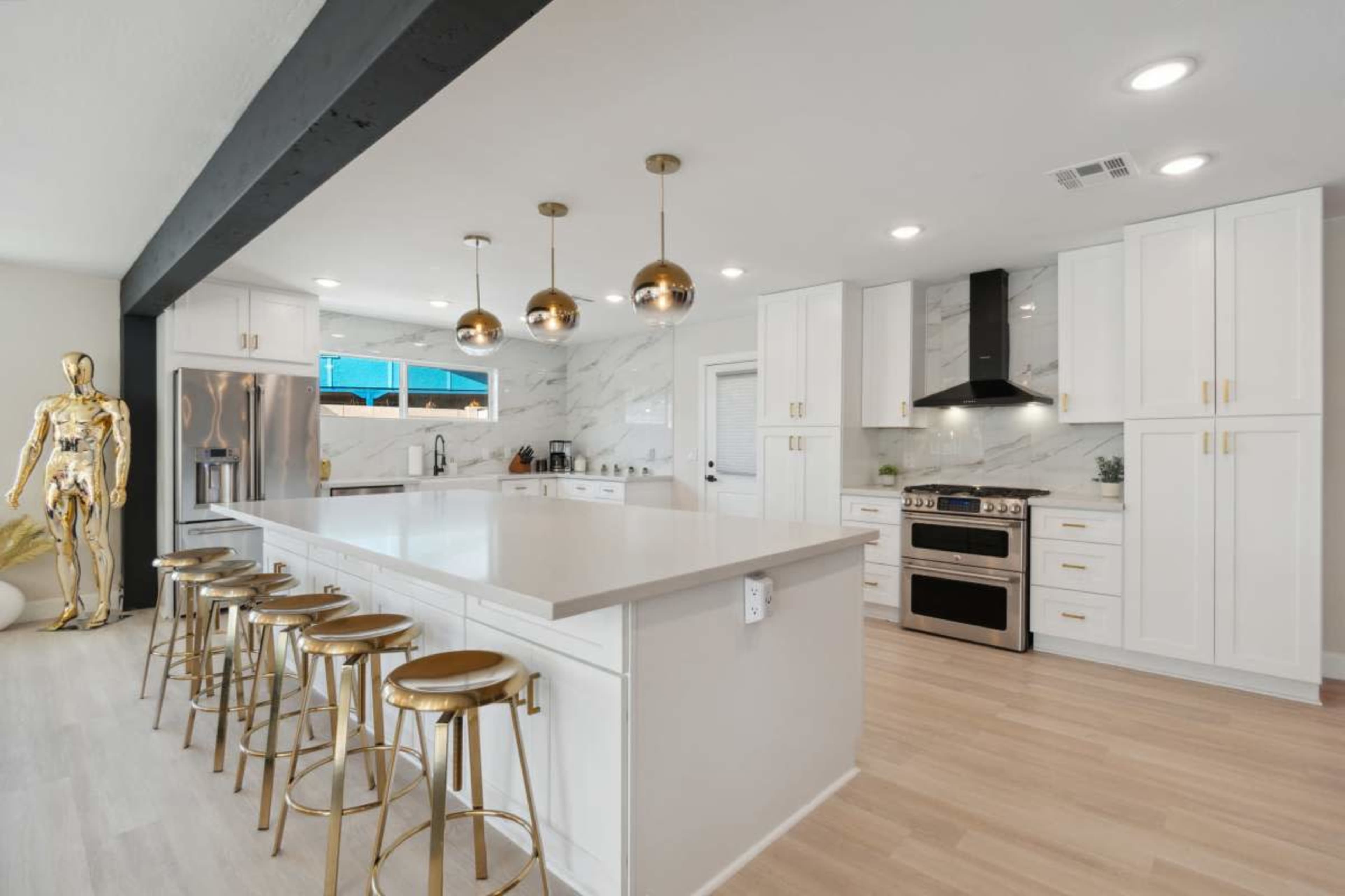 The kitchen features a large central island with barstools, modern appliances, and marble accents.