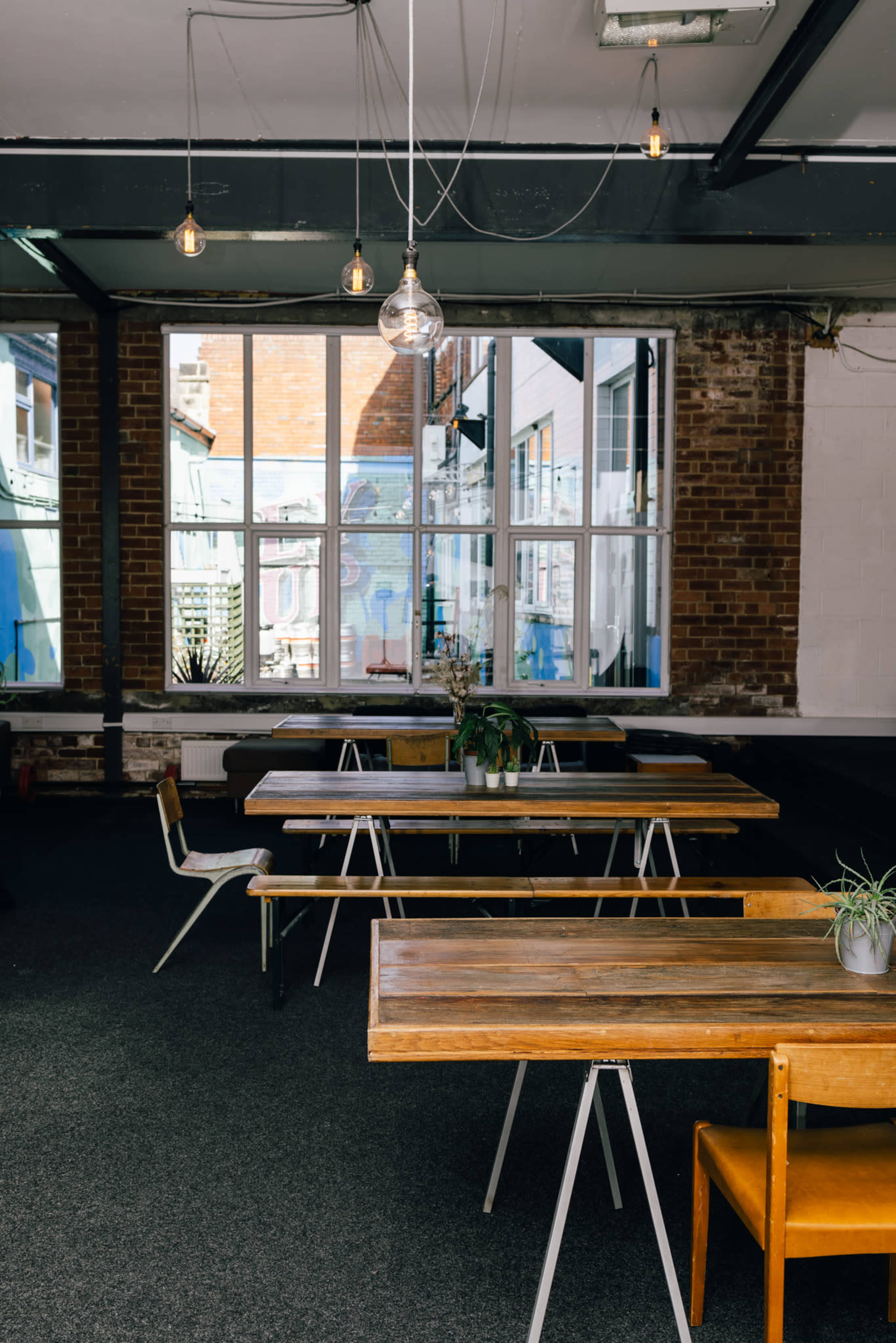 A modern, minimalist café interior with wooden tables and chairs, large windows, and pendant lighting.