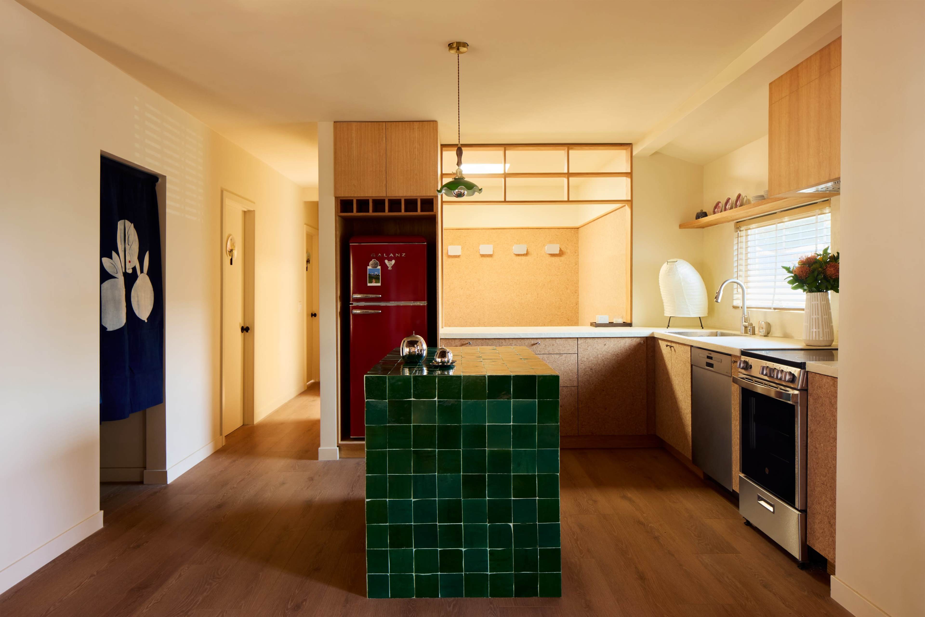 The image shows a modern kitchen featuring a green tiled island, wooden cabinets, and a red refrigerator.
