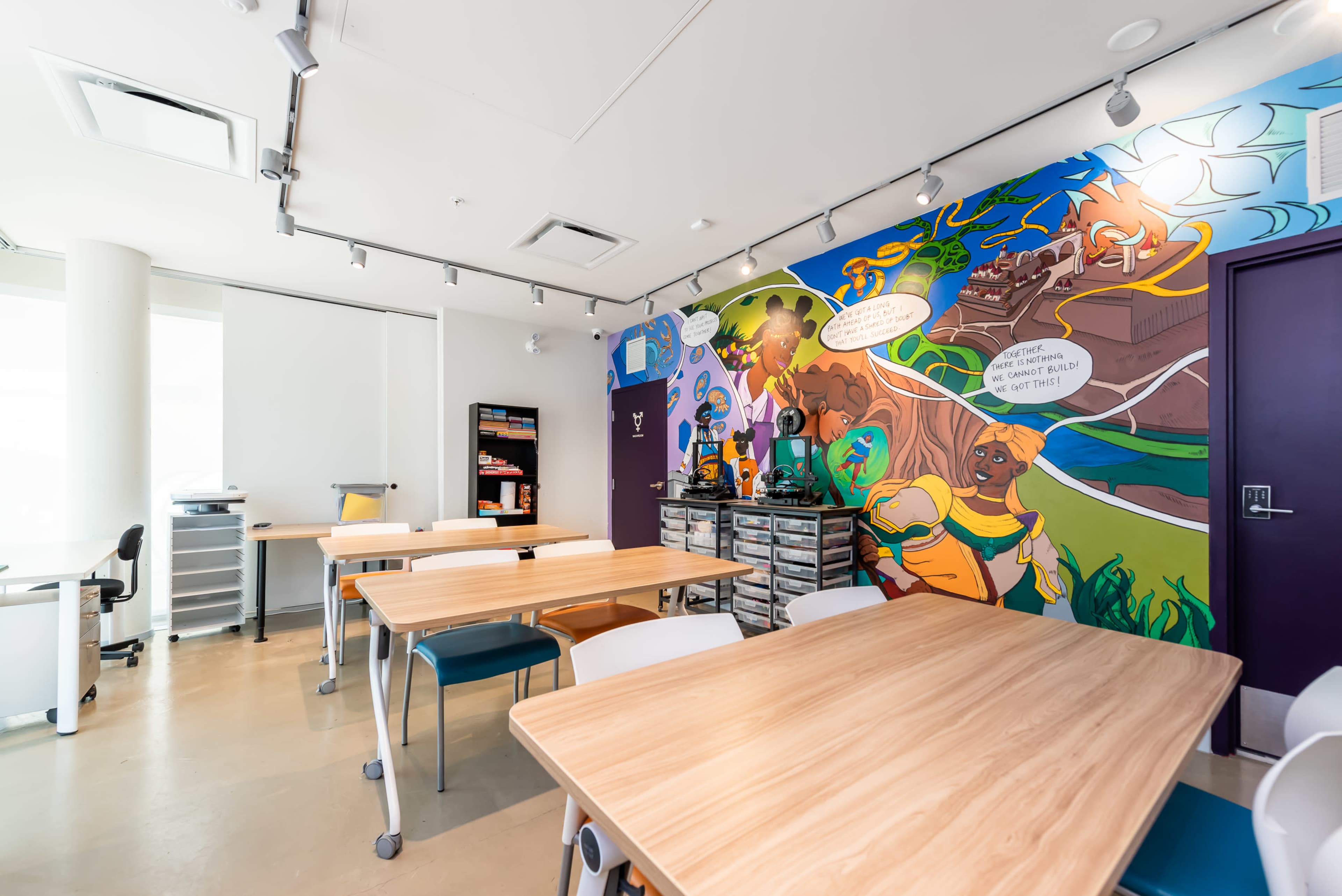 A brightly colored classroom featuring multiple wooden tables and a mural depicting characters and scenes on one wall.
