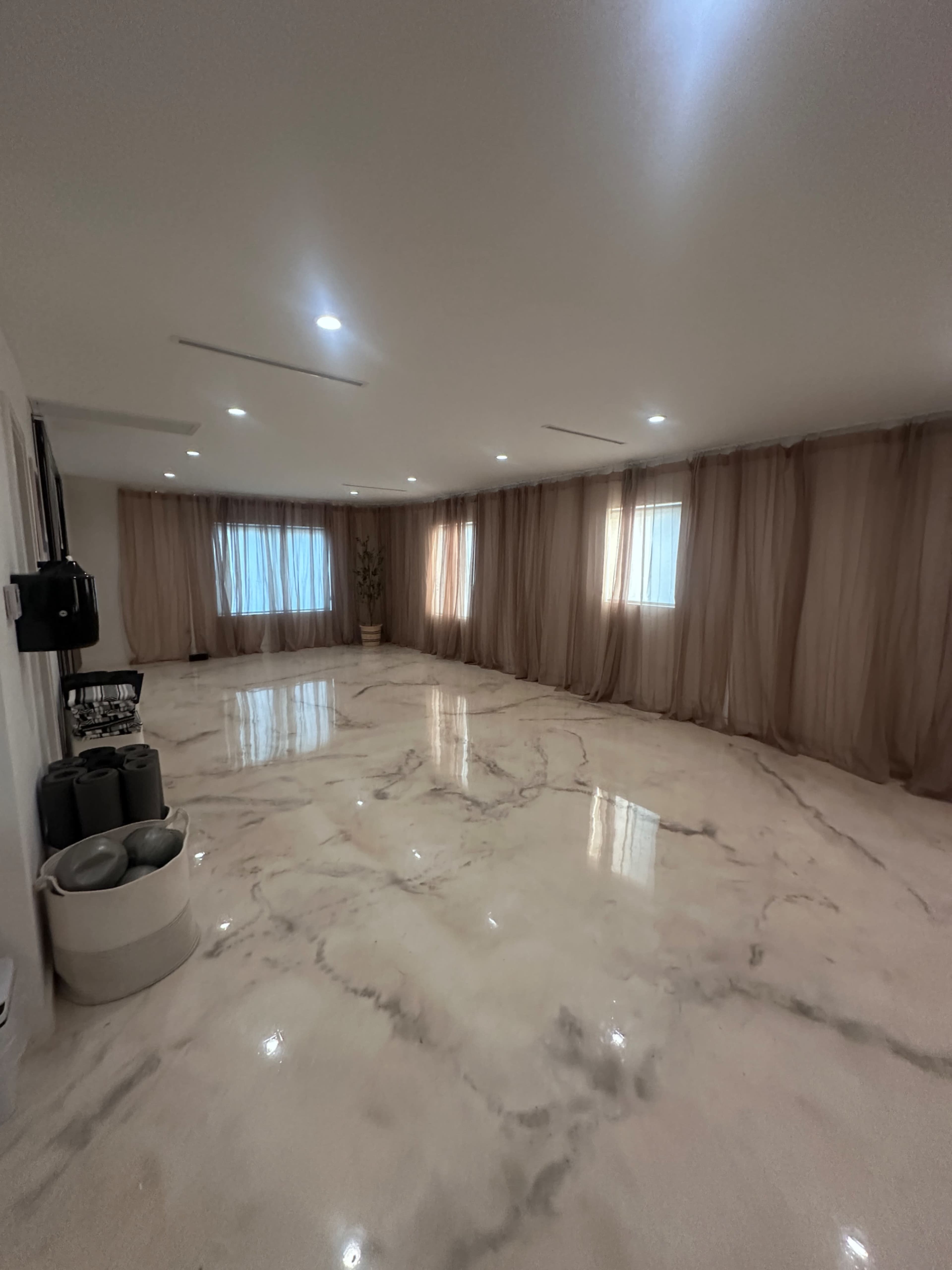 The room features a shiny marble floor, draped fabric curtains, and several windows allowing natural light to enter.
