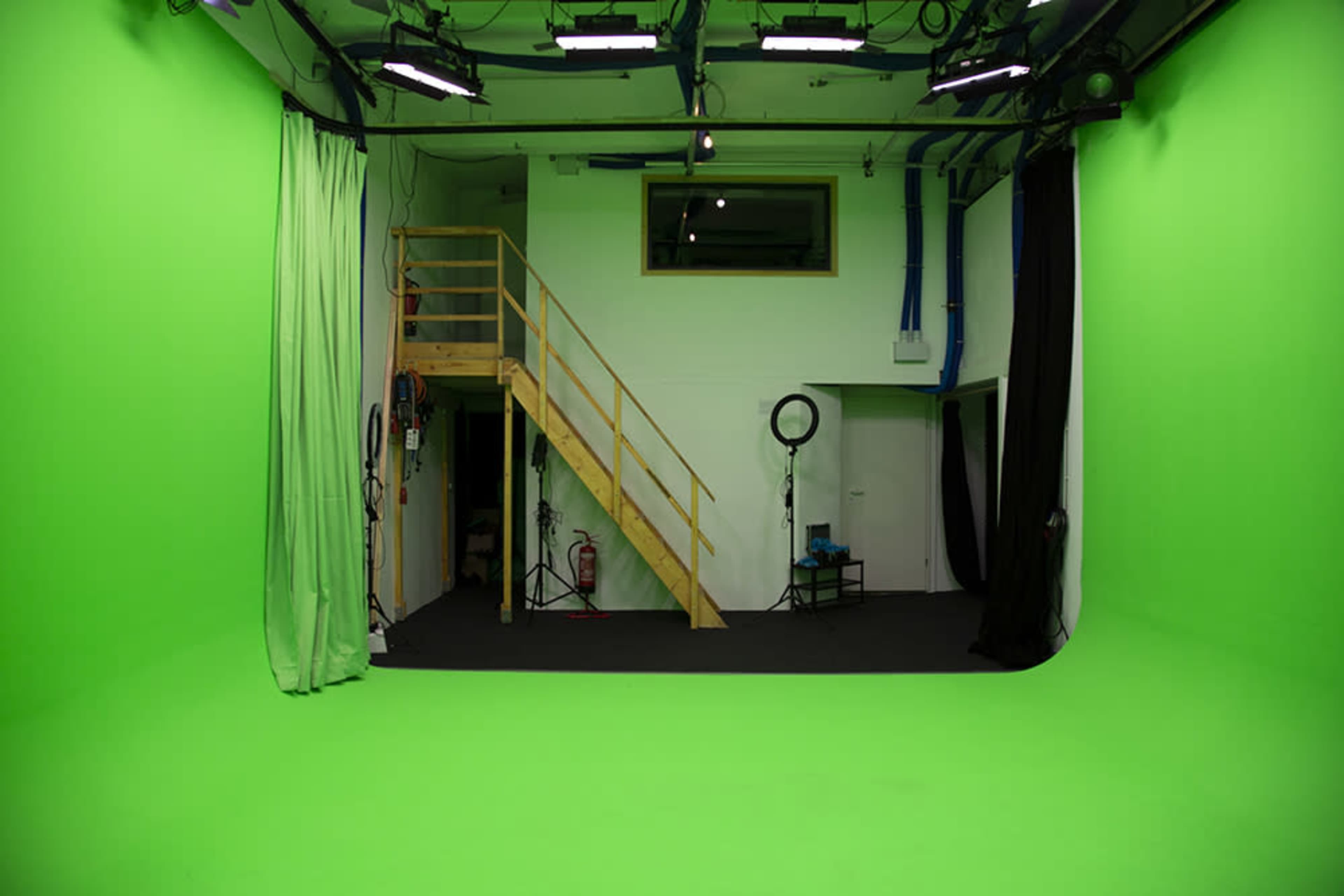 A green screen studio with a staircase leading to an upper level, surrounded by green and black fabric backdrops.