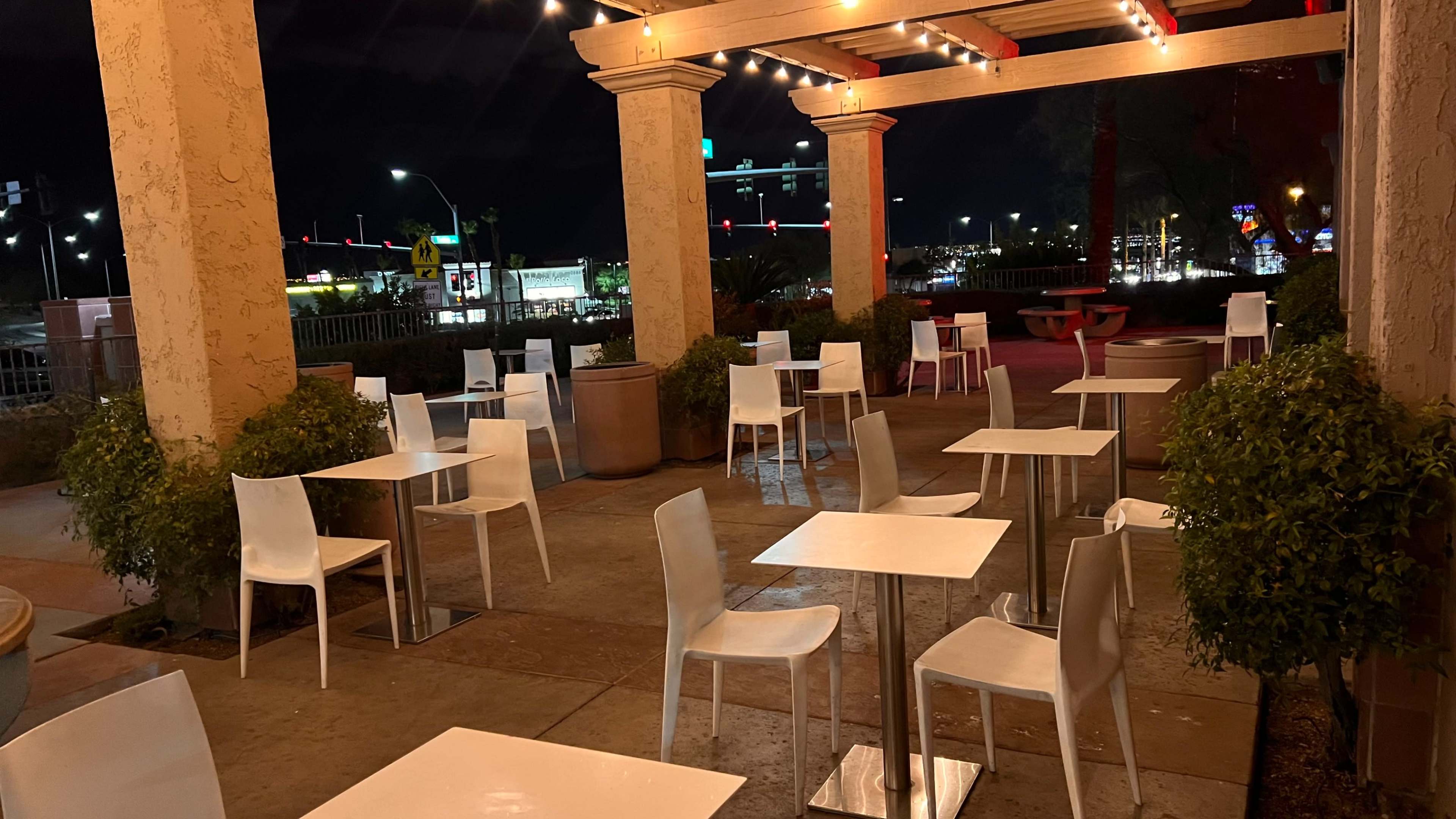 An outdoor dining area at night with several empty white tables and chairs under string lights.