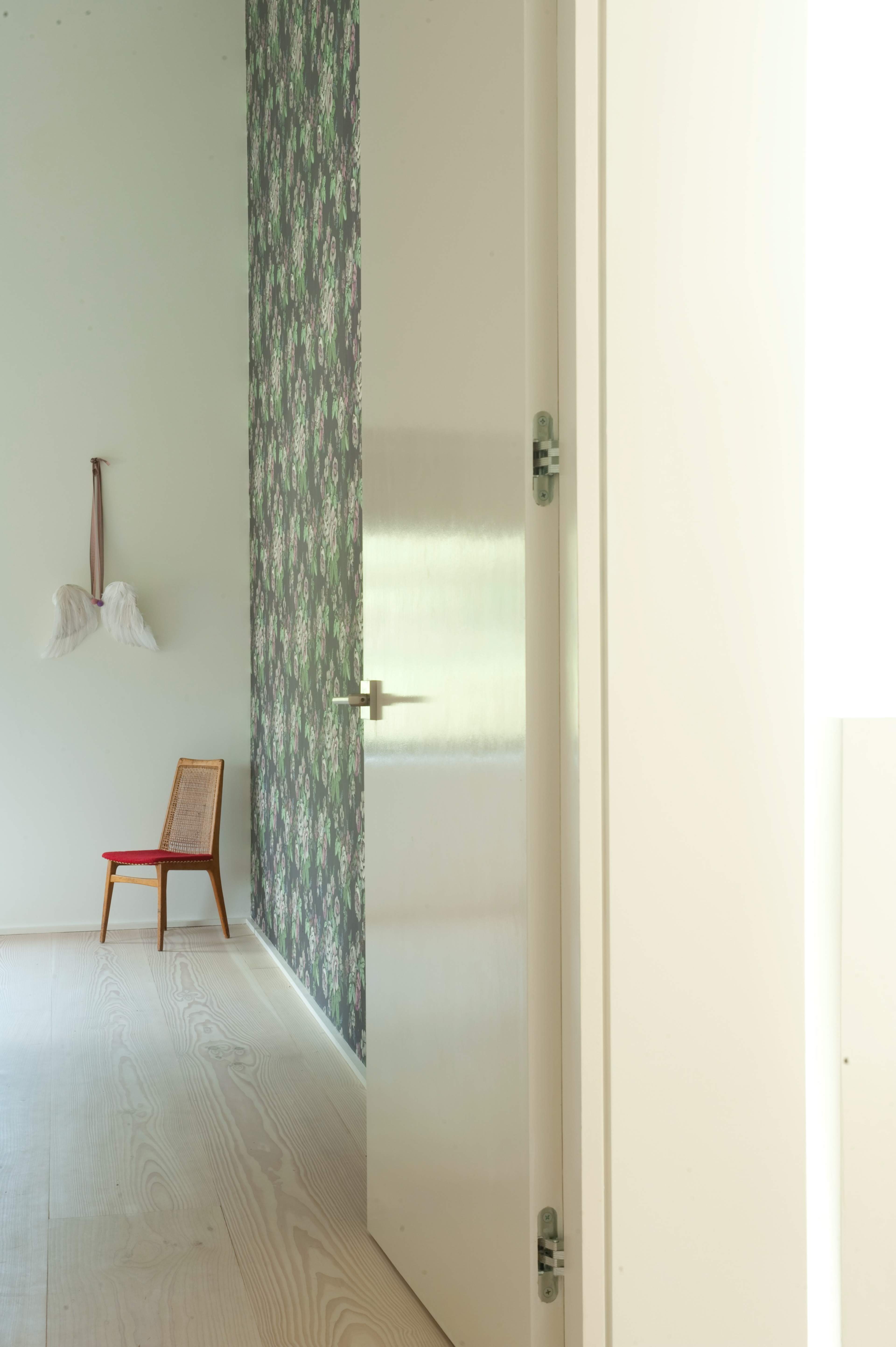 A narrow hallway features a closed door, a floral wallpapered wall, and a wooden chair against the floor.