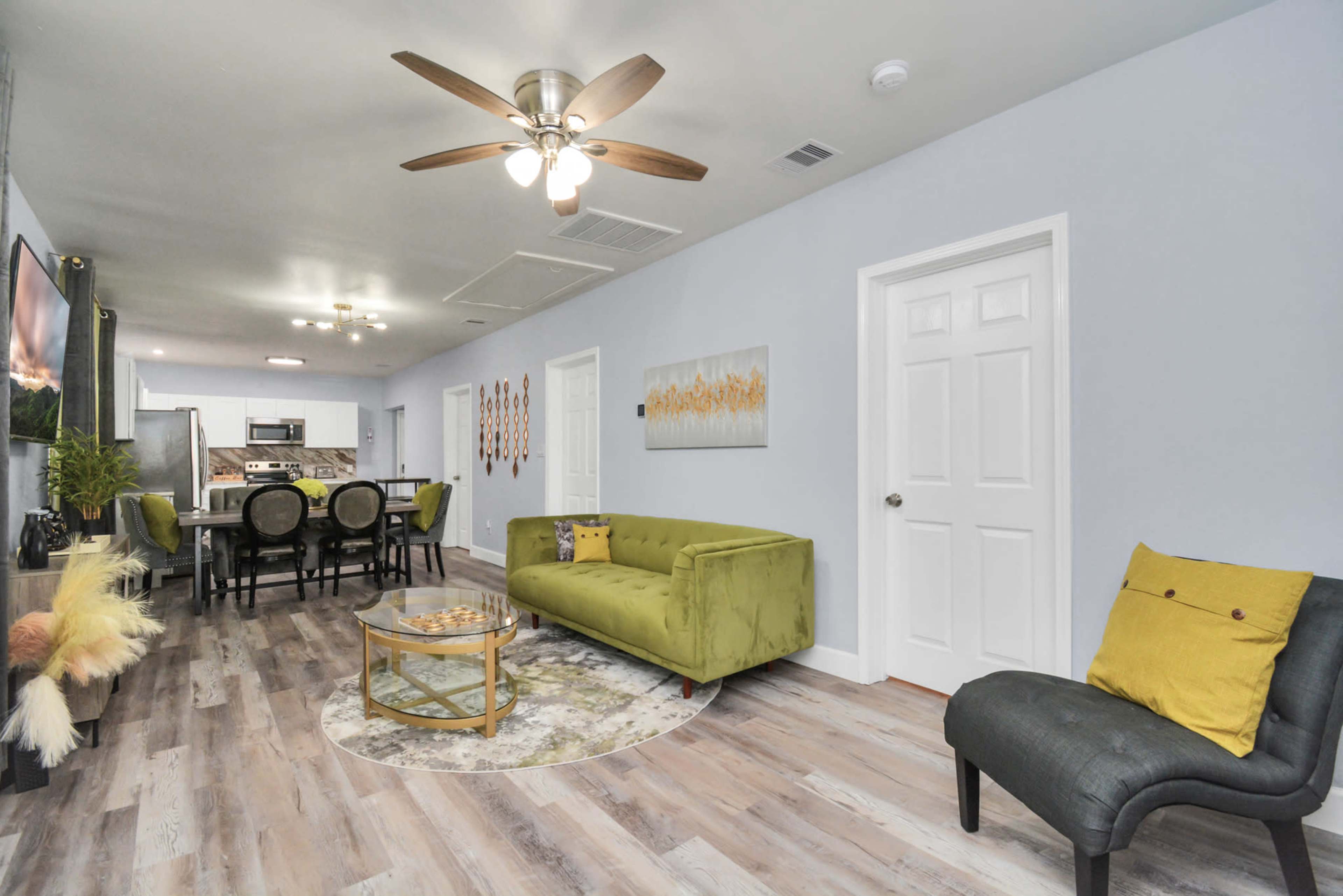 A spacious living area featuring a green sofa, a round rug, and a dining area visible in the background with modern furnishings.
