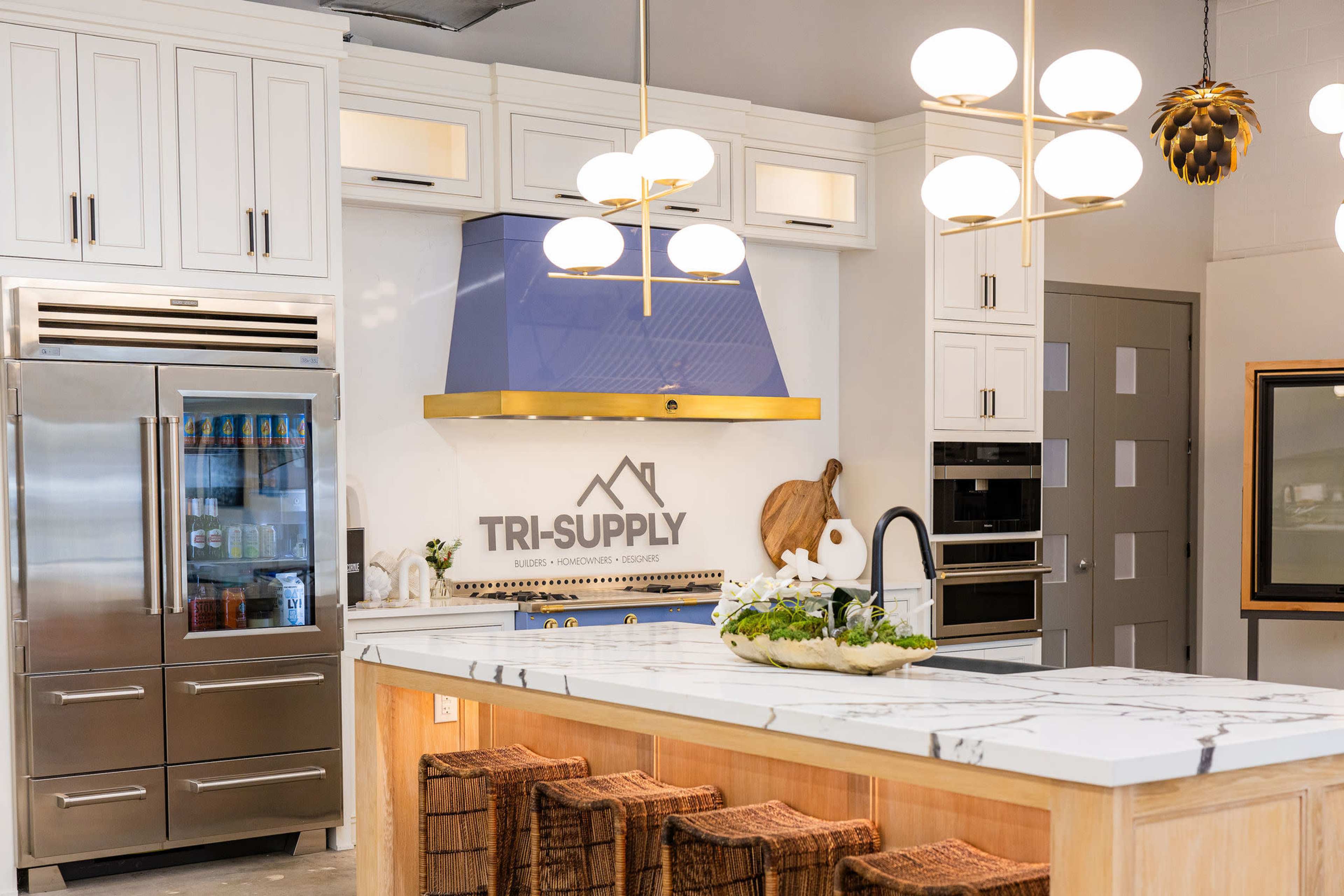 The image shows a modern kitchen featuring stainless steel appliances, a blue hood above the stove, and a large island with a marble countertop.