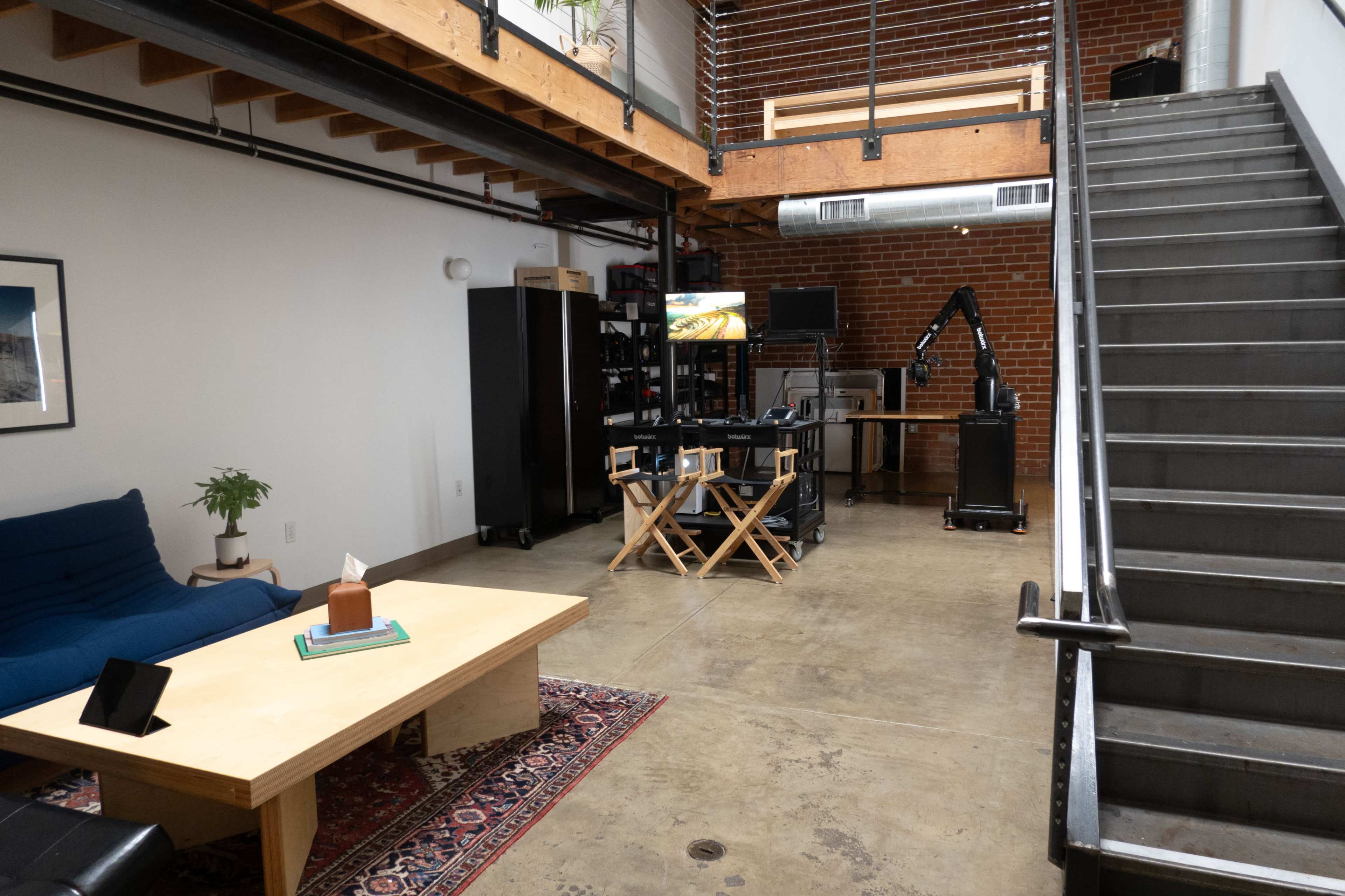 A spacious loft-like interior with a blue couch, a wooden coffee table, and a staircase leading to an upper level.