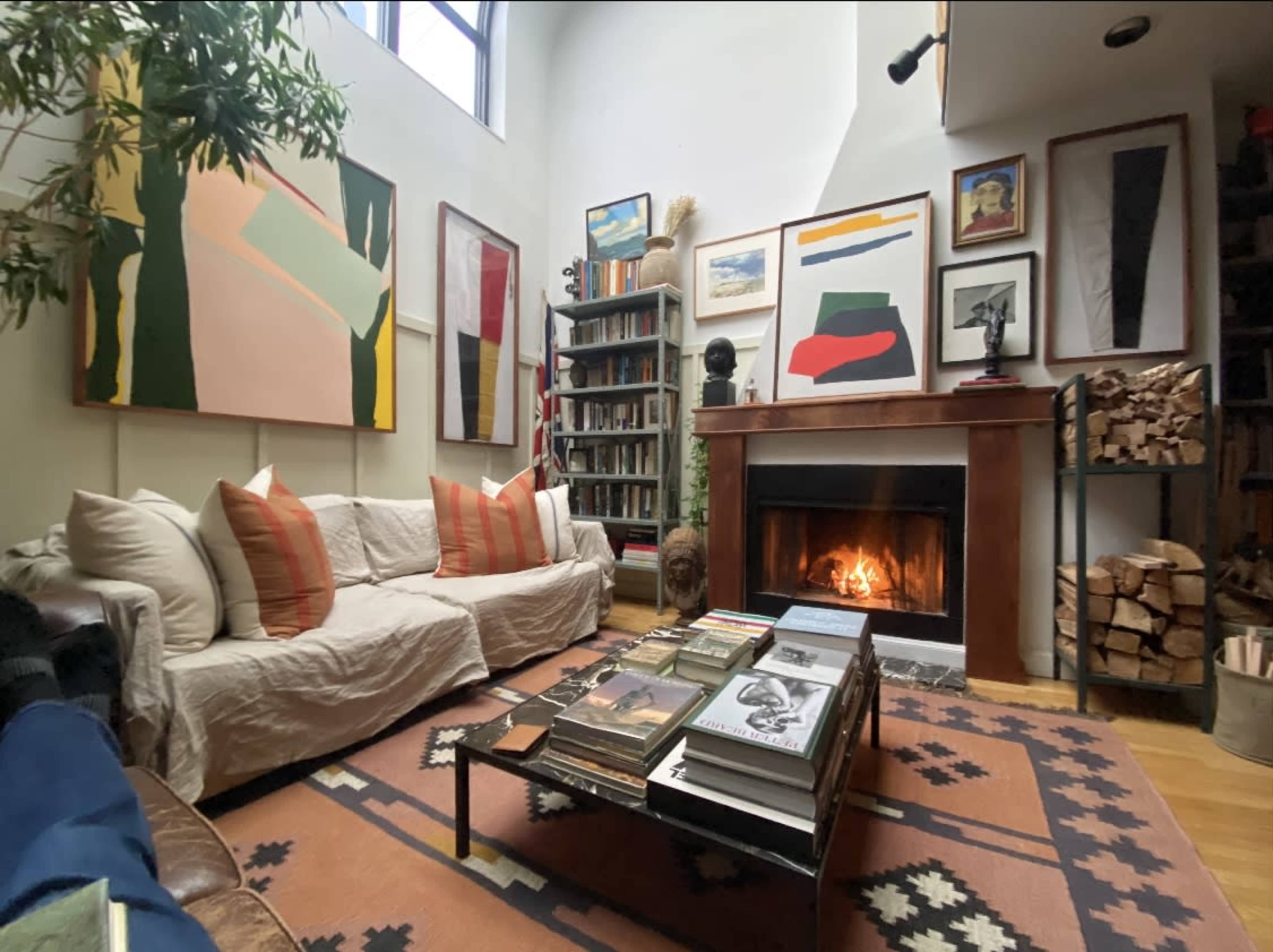 The image depicts a cozy living room with a sofa, a bookshelf filled with books, a fireplace with a fire burning, and artwork hanging on the walls.