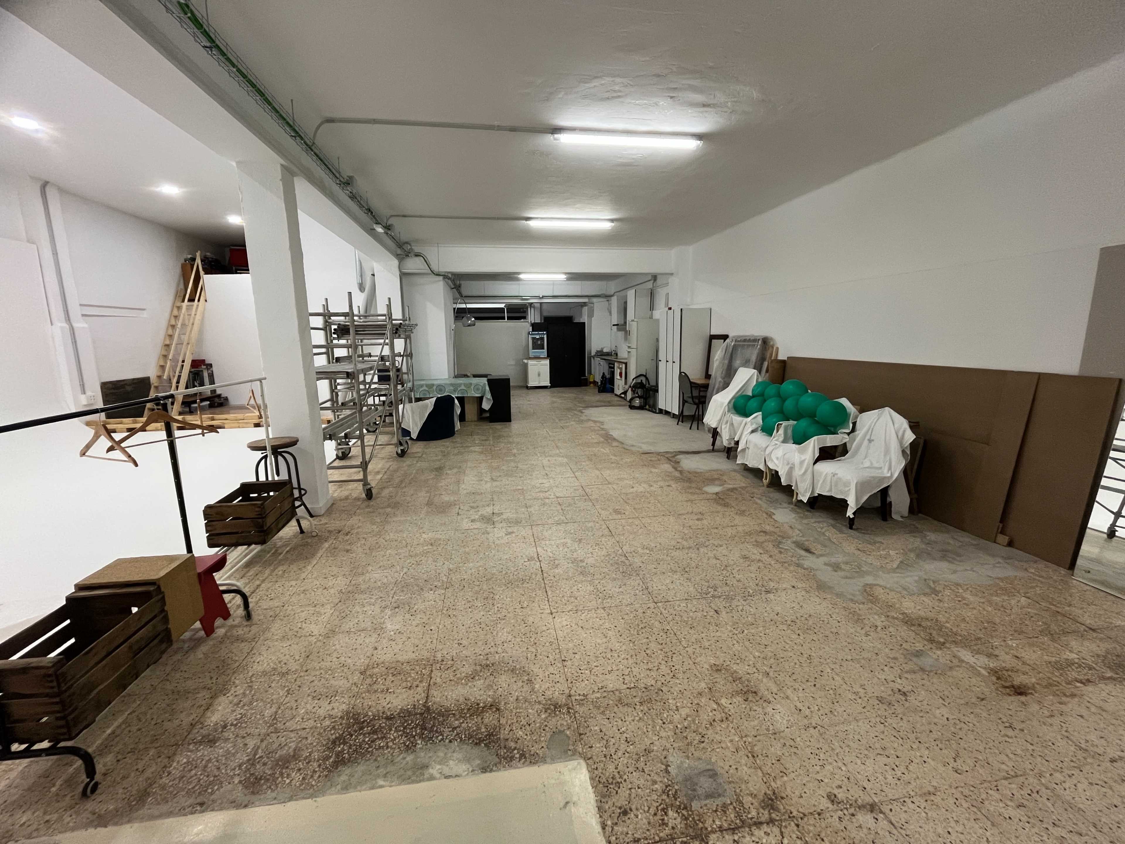 The image shows a spacious, unfinished interior with scattered furniture, green objects covered with white cloths, and equipment along the walls.