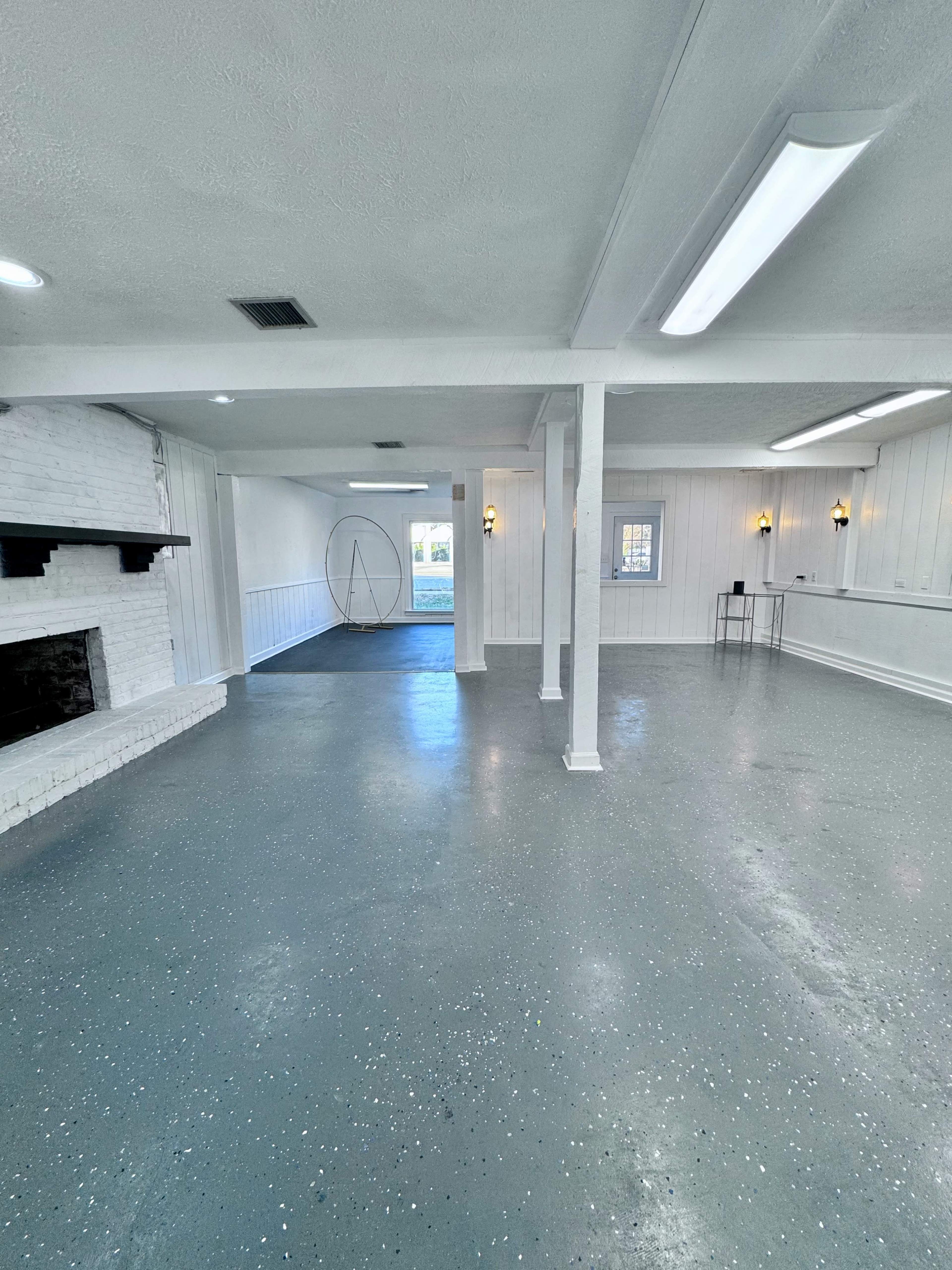 An empty, well-lit indoor space with white walls, a fireplace on one side, and a circular stand in the center.