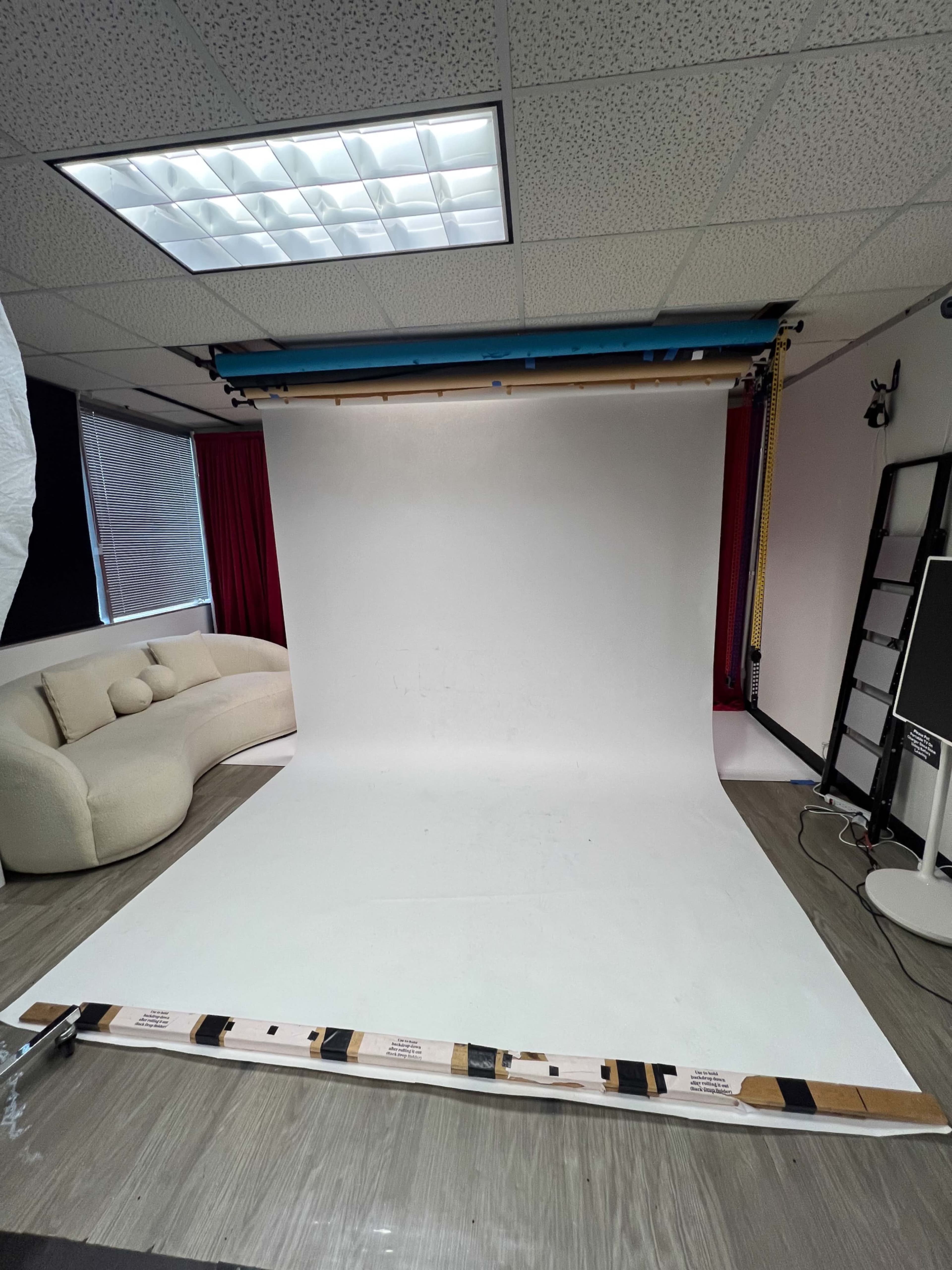 The image shows an empty photography studio with a white backdrop, a curved floor, and a soft couch in the corner.