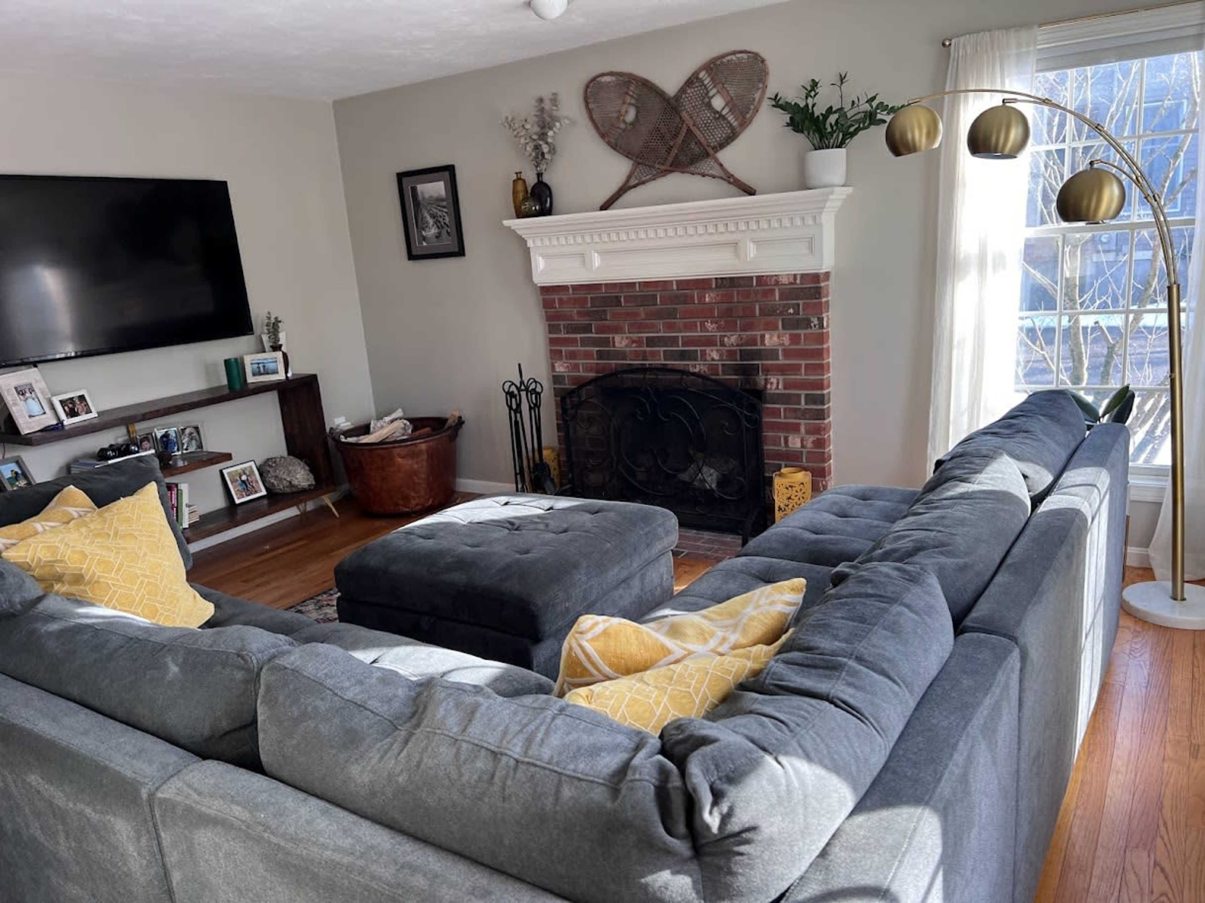 The living room features a gray sectional sofa, a brick fireplace, and a large television on a shelf, with decorative items on display.