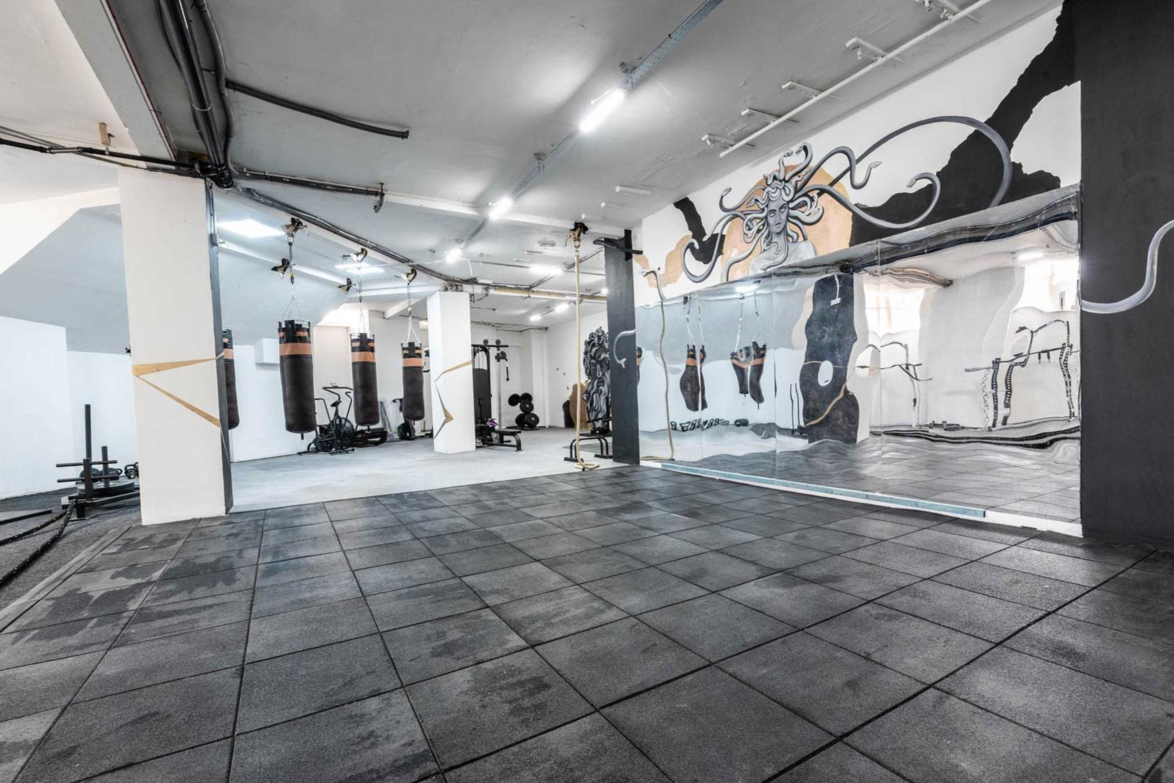 A spacious gym interior featuring rubber flooring, wall mirrors, and exercise equipment along with a mural of an octopus.
