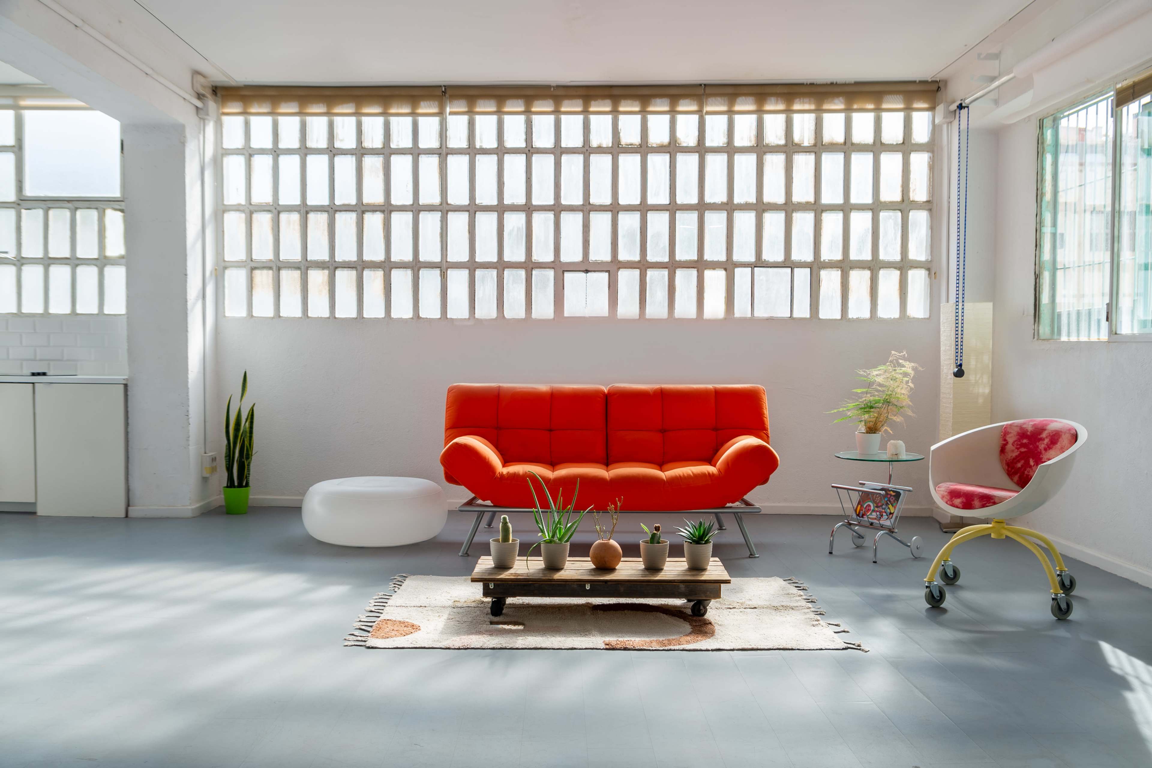 A bright, modern living space featuring an orange sofa, a low coffee table with decorative items, and large windows letting in natural light.