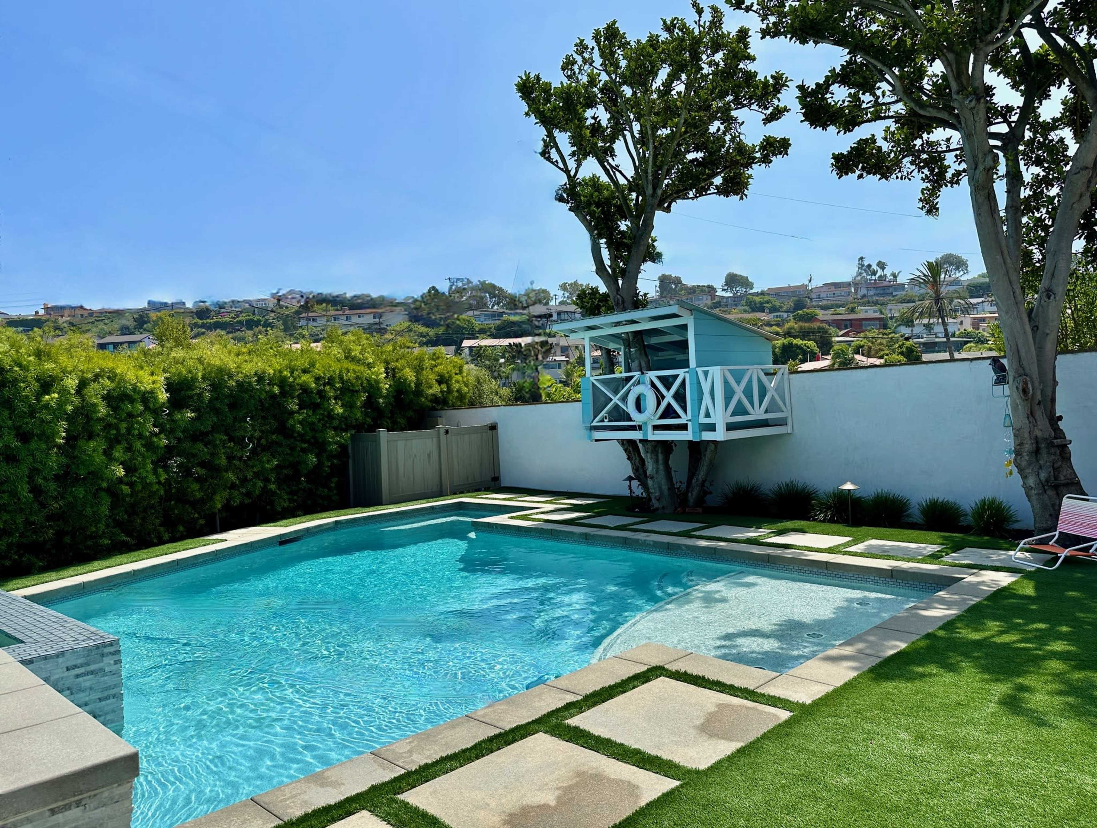 The image shows a residential backyard with a swimming pool, a small blue pool house, and landscaped greenery.