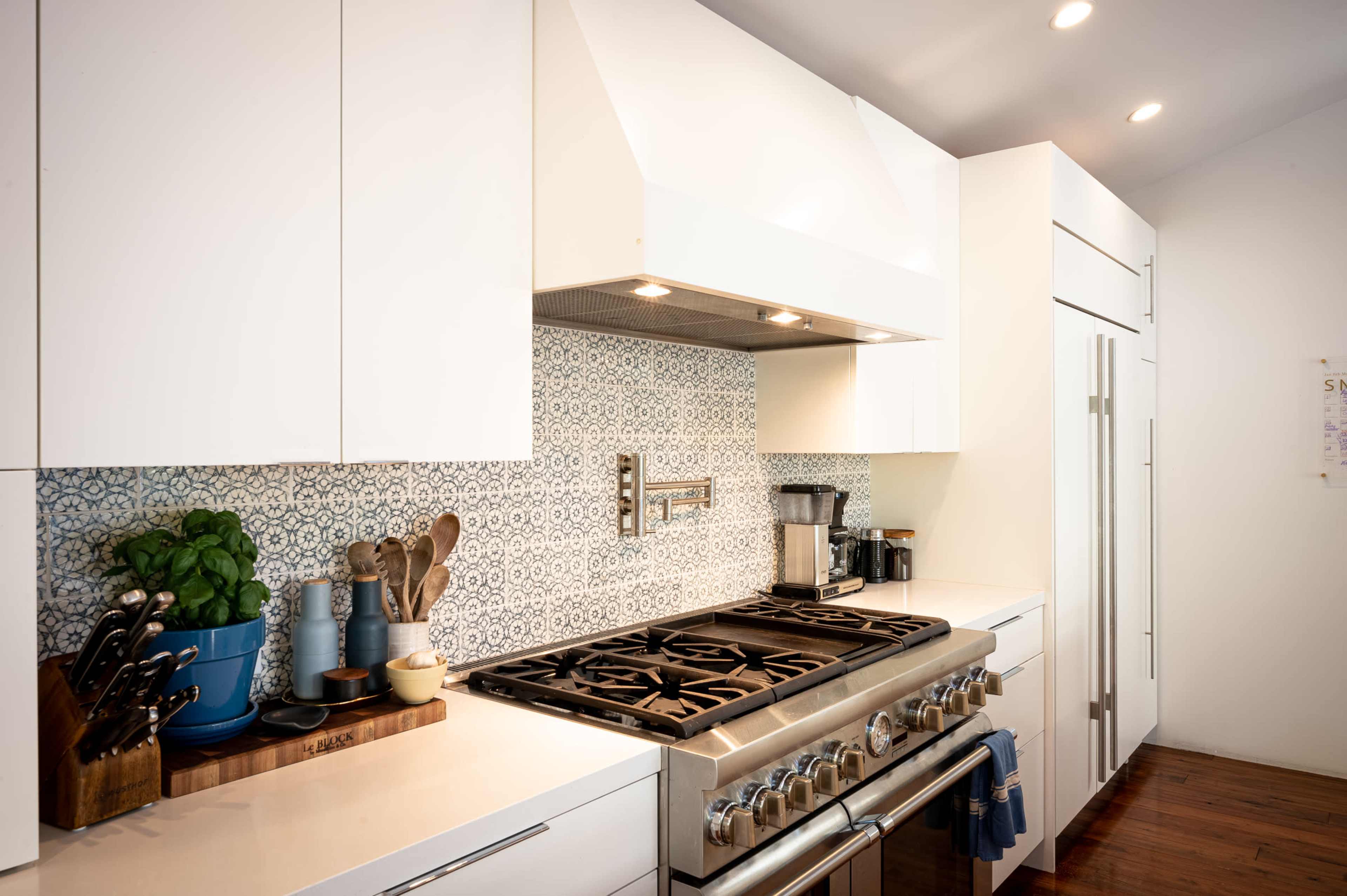A modern kitchen features a gas range with a patterned backsplash, white cabinetry, and a coffee maker on the counter.