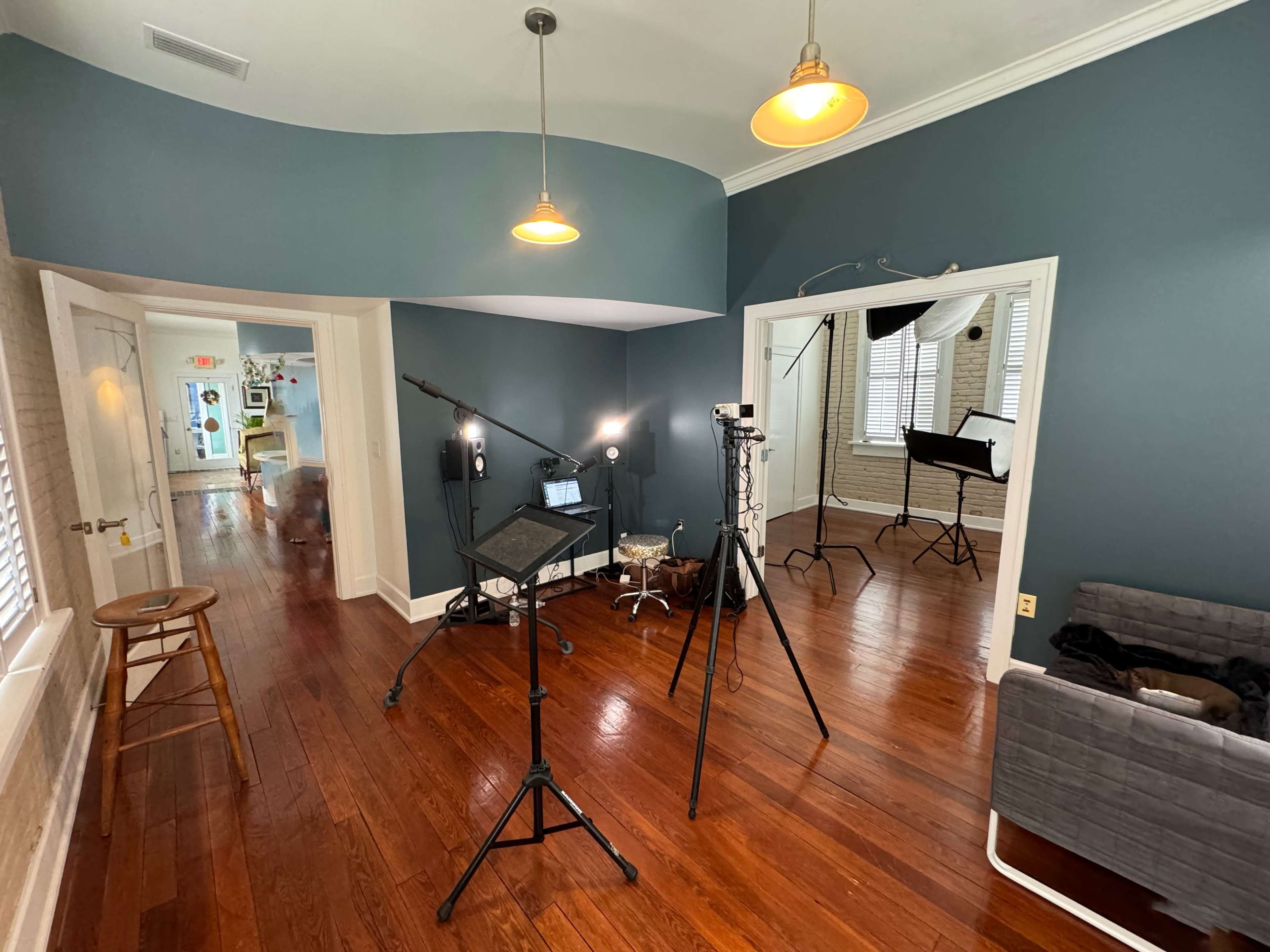A well-lit room with wooden floors, featuring various photography equipment, including tripods and lighting setups, arranged around a seating area.