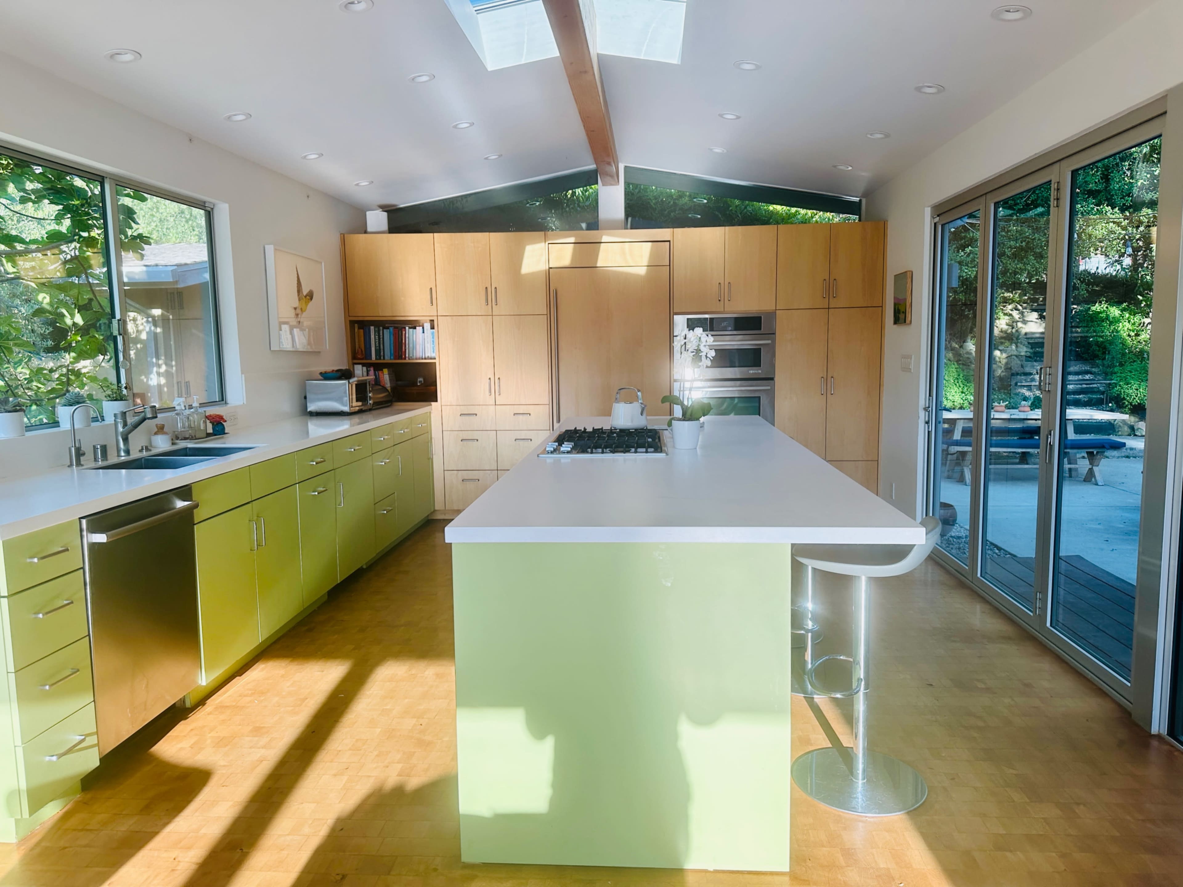 The kitchen features a large central island with a cooktop, surrounded by modern cabinetry and large windows that let in natural light.