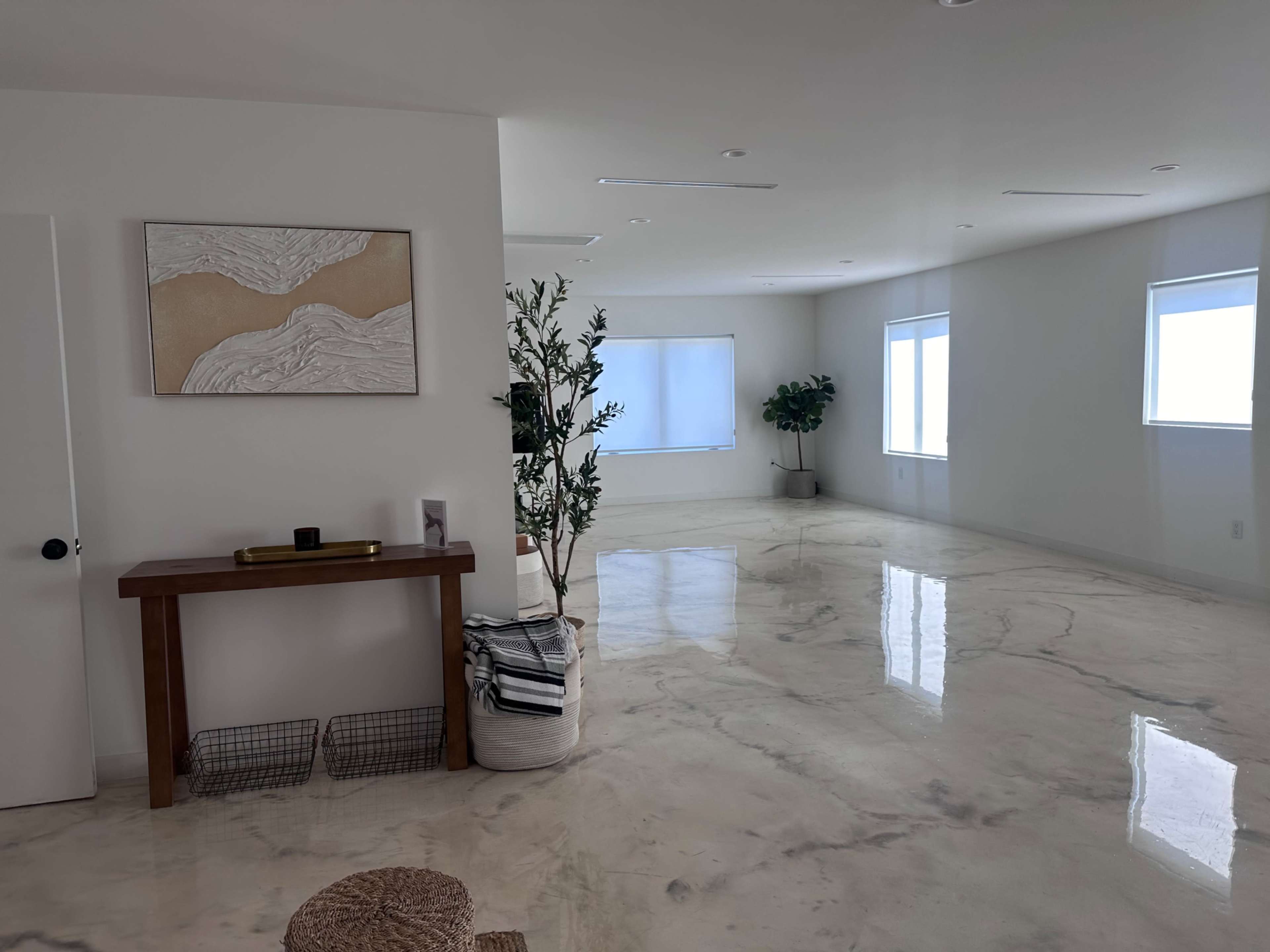 The image shows a spacious, modern room with a glossy marble floor, minimalistic furniture, and natural light coming through large windows.