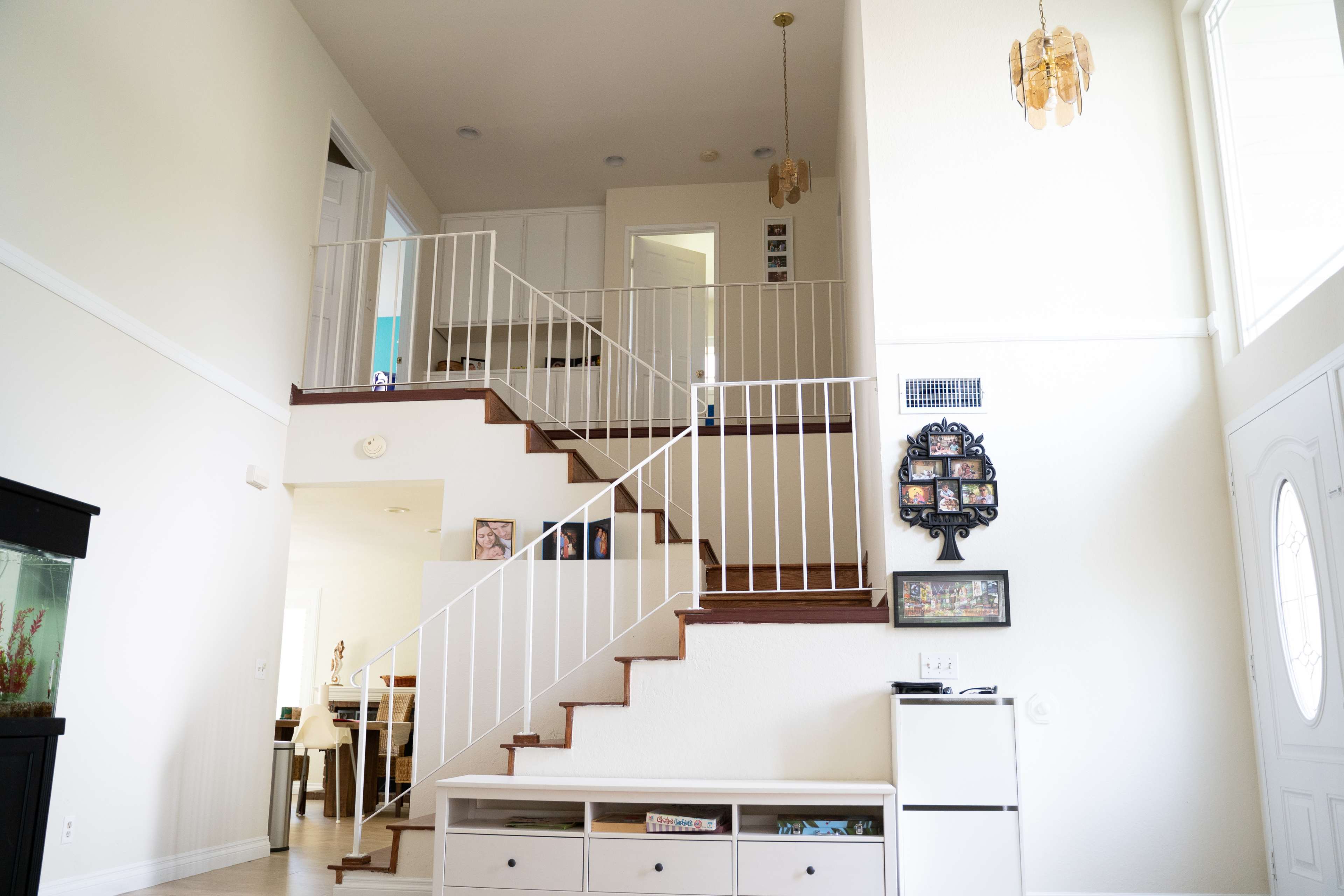 A bright interior entryway with a staircase leading to an upper level, flanked by a white railing and a storage unit below.