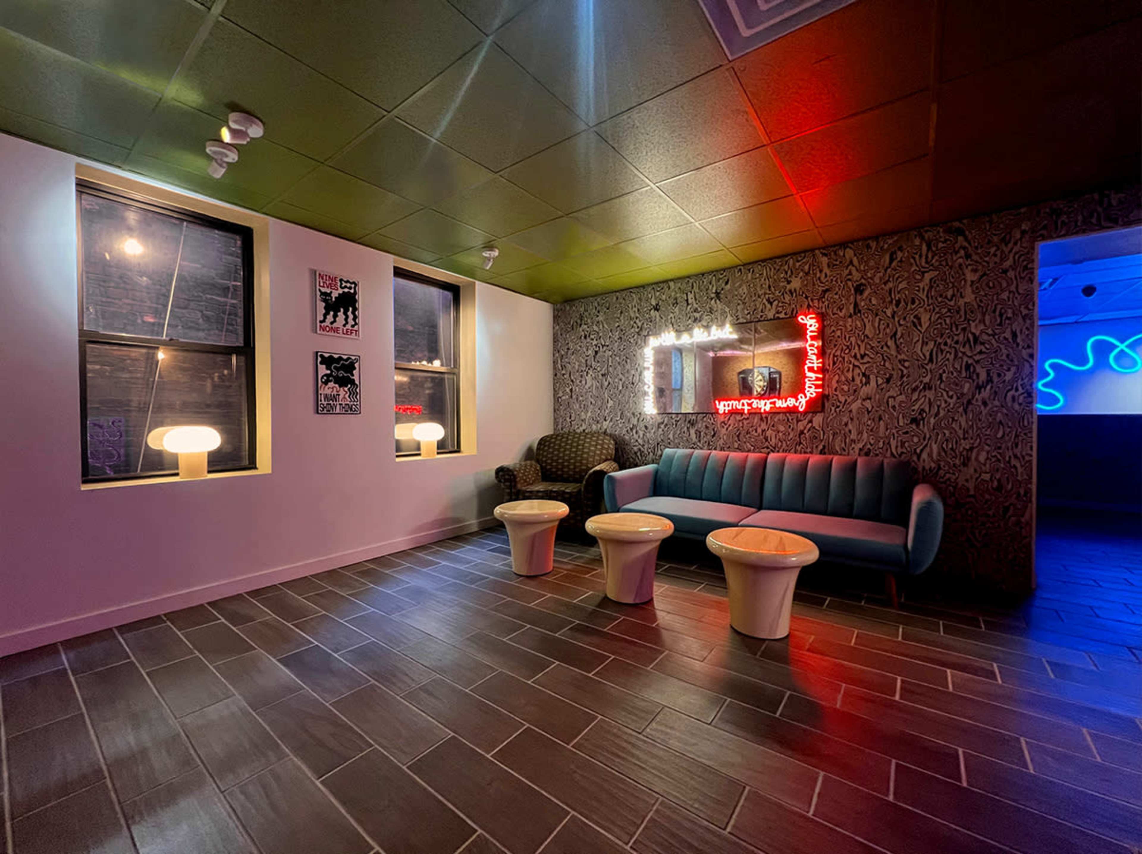 The image shows a modern lounge area with a blue sofa, two white tables, and illuminated wall decor, set against a patterned wallpaper and contrasting ceiling.