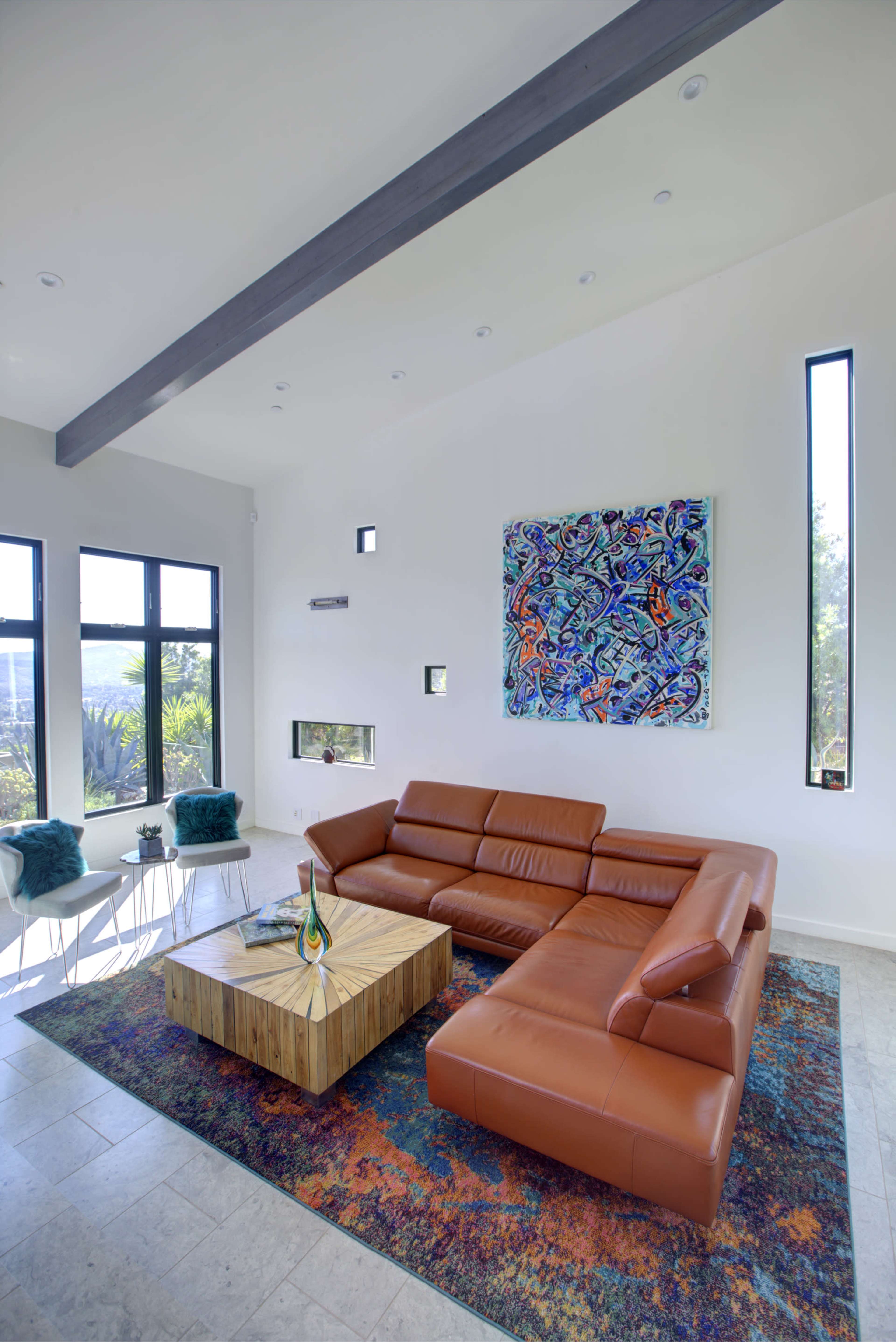 A modern living room features a brown sectional sofa, a wooden coffee table, and abstract artwork on the wall, with large windows allowing natural light in.