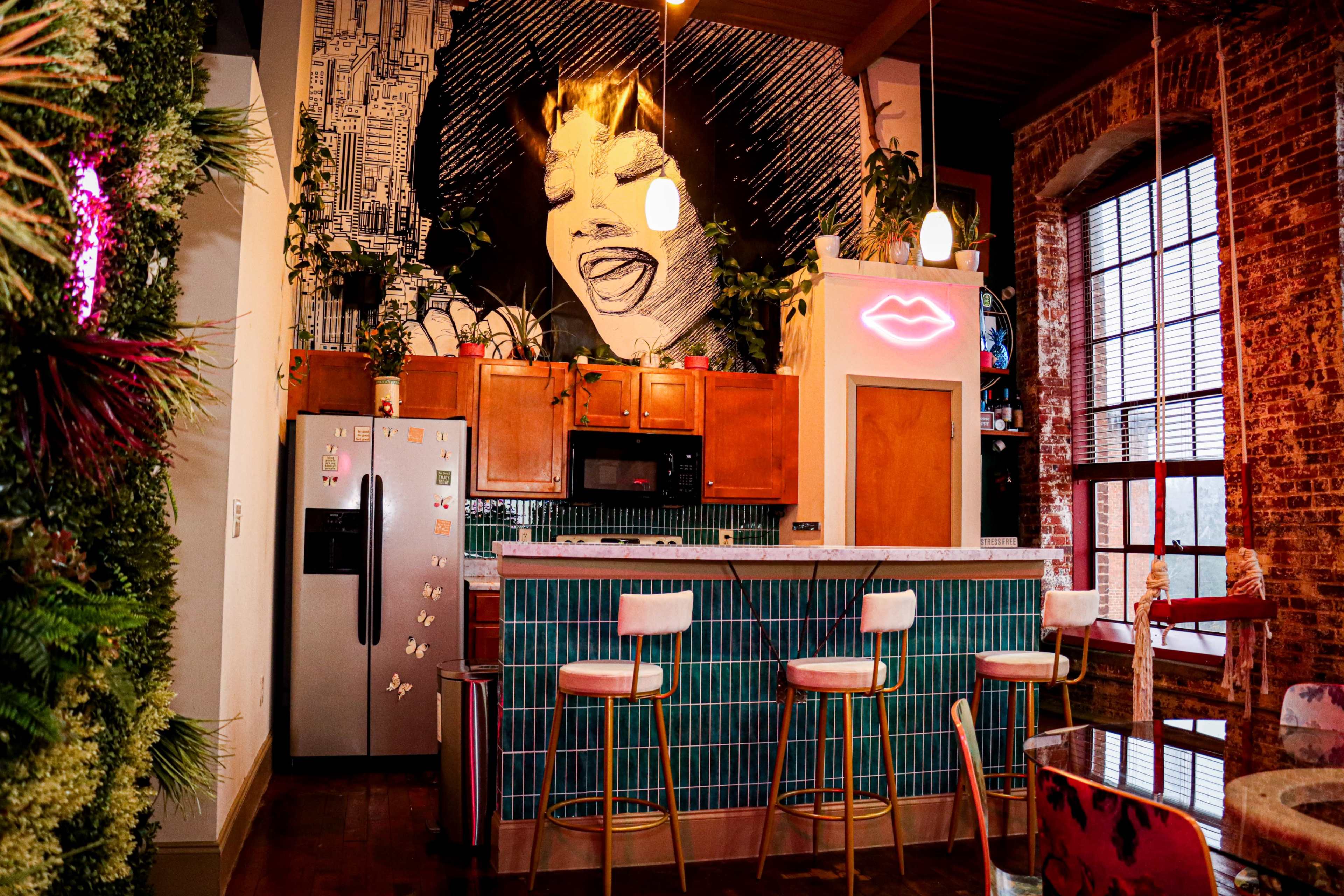 A stylish kitchen with a large mural of a smiling woman, modern bar stools, and a blend of brick and greenery.