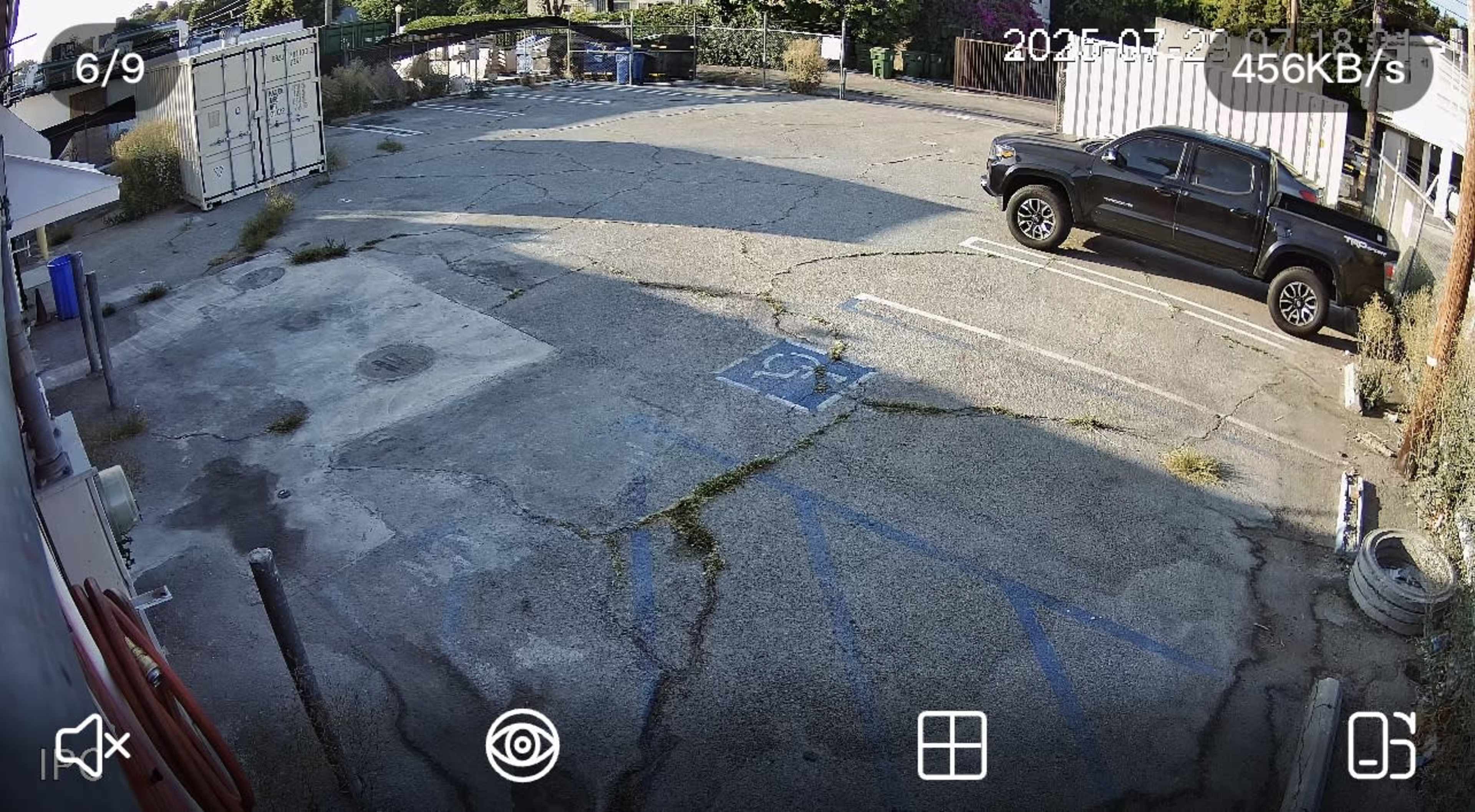 The image shows an empty parking lot with a black pickup truck parked on the right side and several shipping containers in the background.