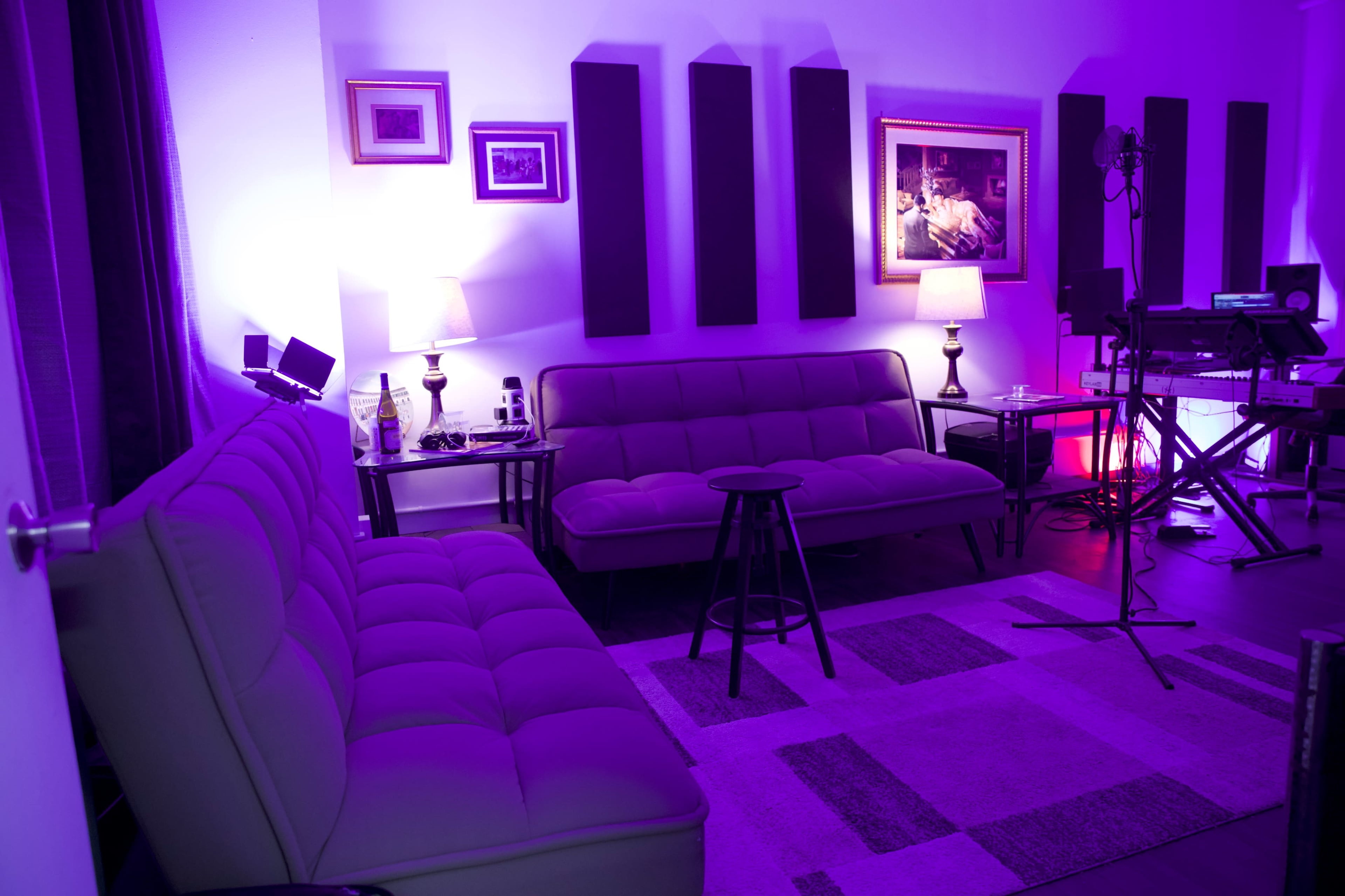 The image shows a dimly lit lounge area with two sofas, side tables with lamps, and soundproofing panels on the walls.