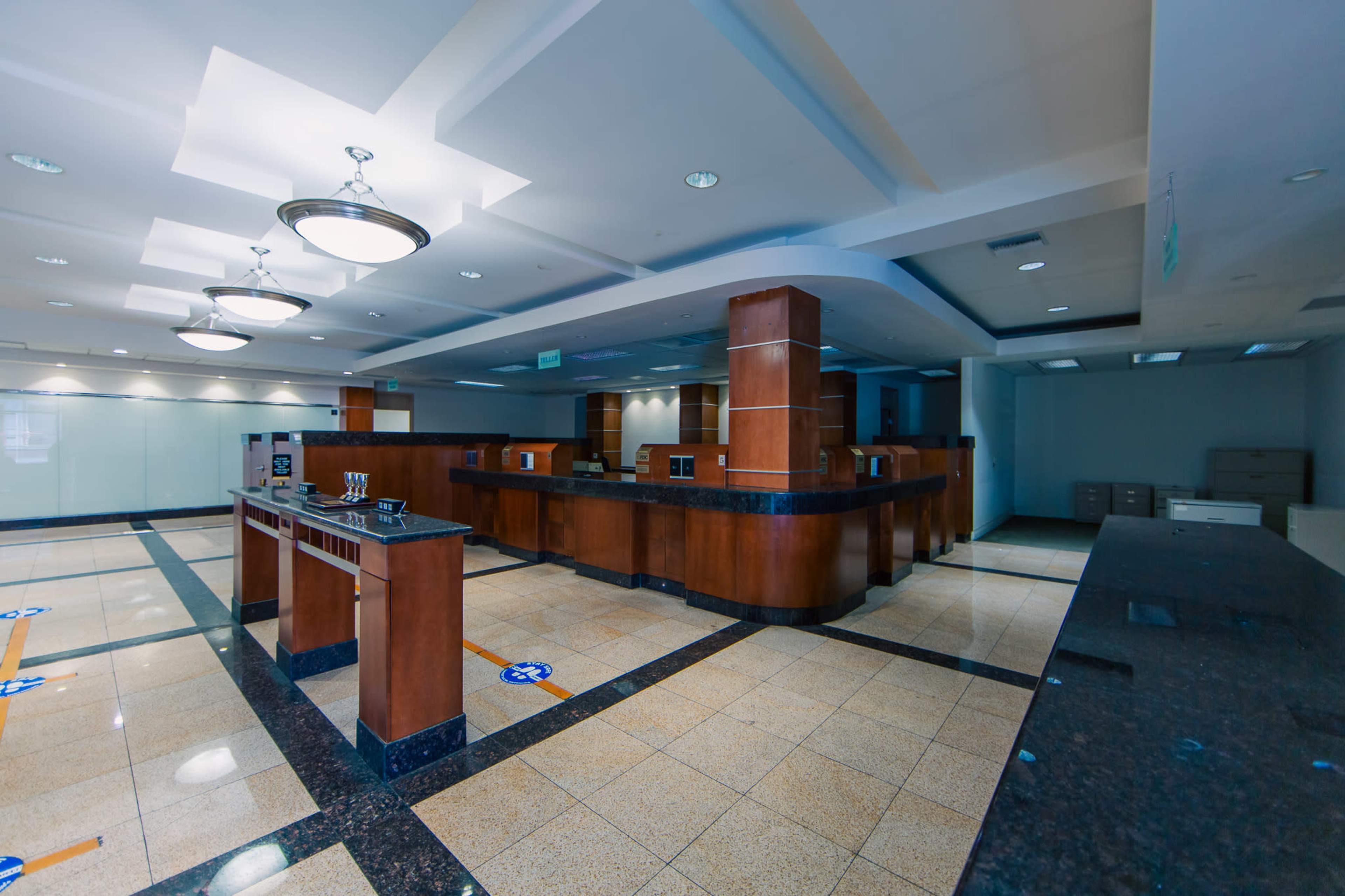 The image shows an empty office space with wooden reception counters, polished tile flooring, and overhead lighting.