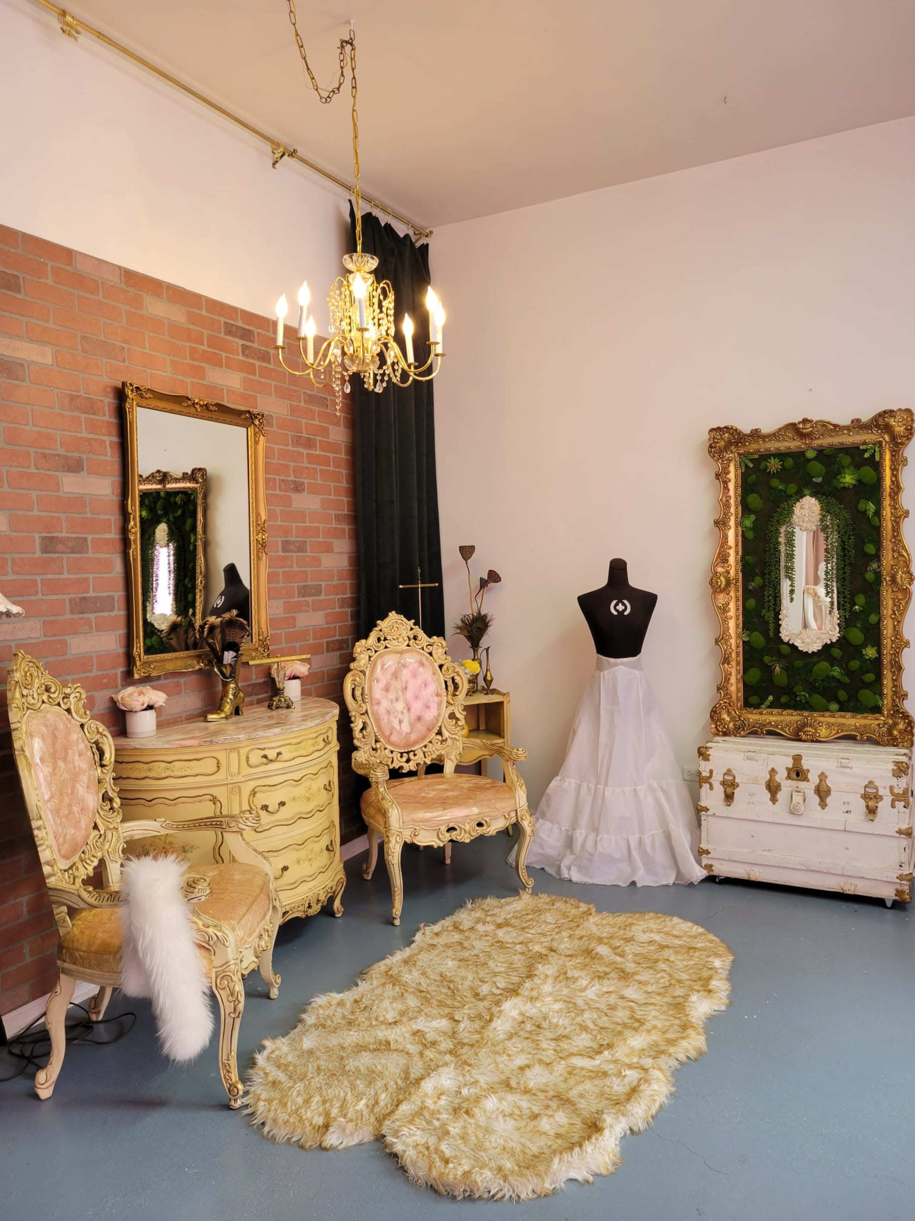 The room features ornate golden furniture, including chairs and a dresser, accented by a large mirror and a mannequin, all set against a backdrop of brick walls and a plush rug.