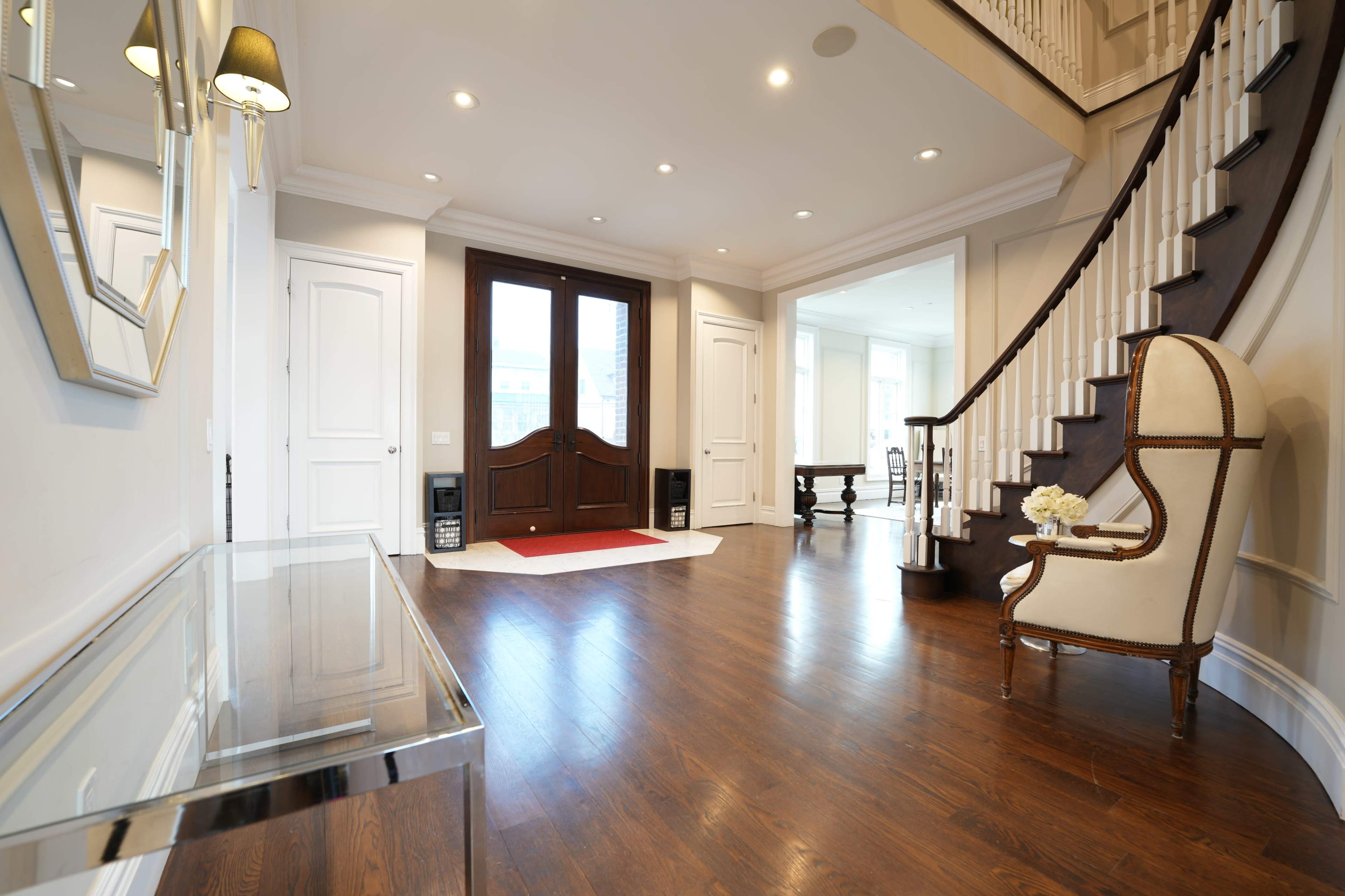 The entryway features a staircase, an ornate chair, and a large front door with sidelights, accompanied by a sleek console table and polished wooden floors.