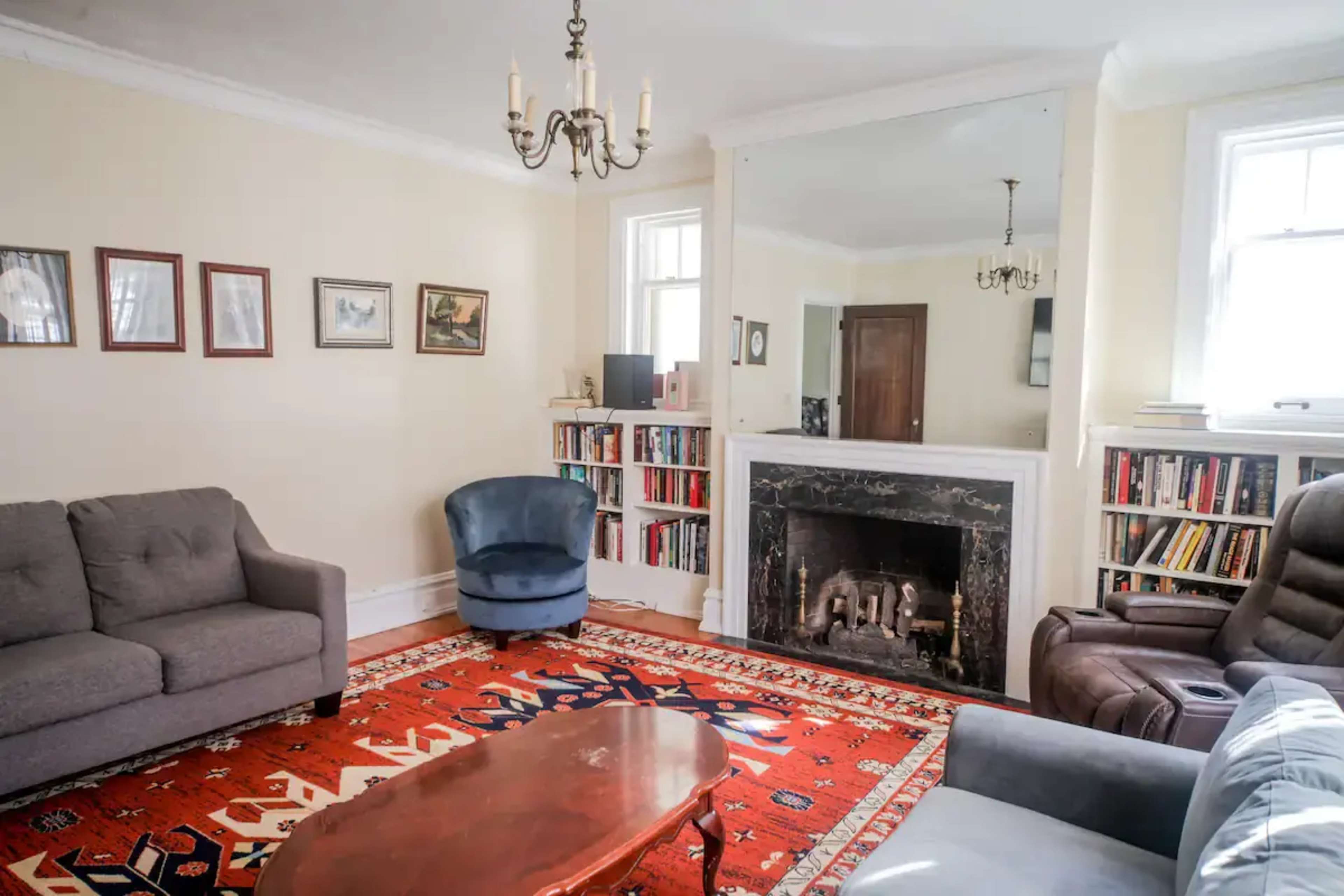 A living room with a patterned rug, two sofas, an armchair, a wooden coffee table, and a fireplace with a large mirror above it.