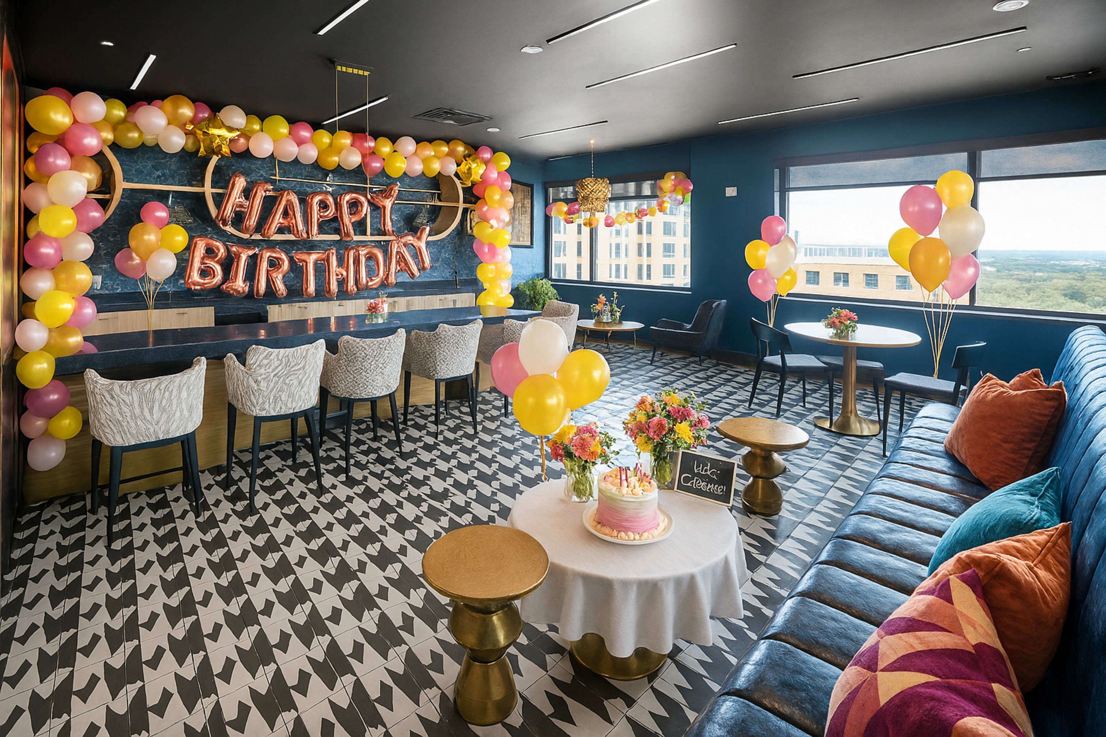 The image shows a decorated birthday celebration venue featuring colorful balloons, a "Happy Birthday" sign, a cake on a table, and seating arrangements with a modern design.