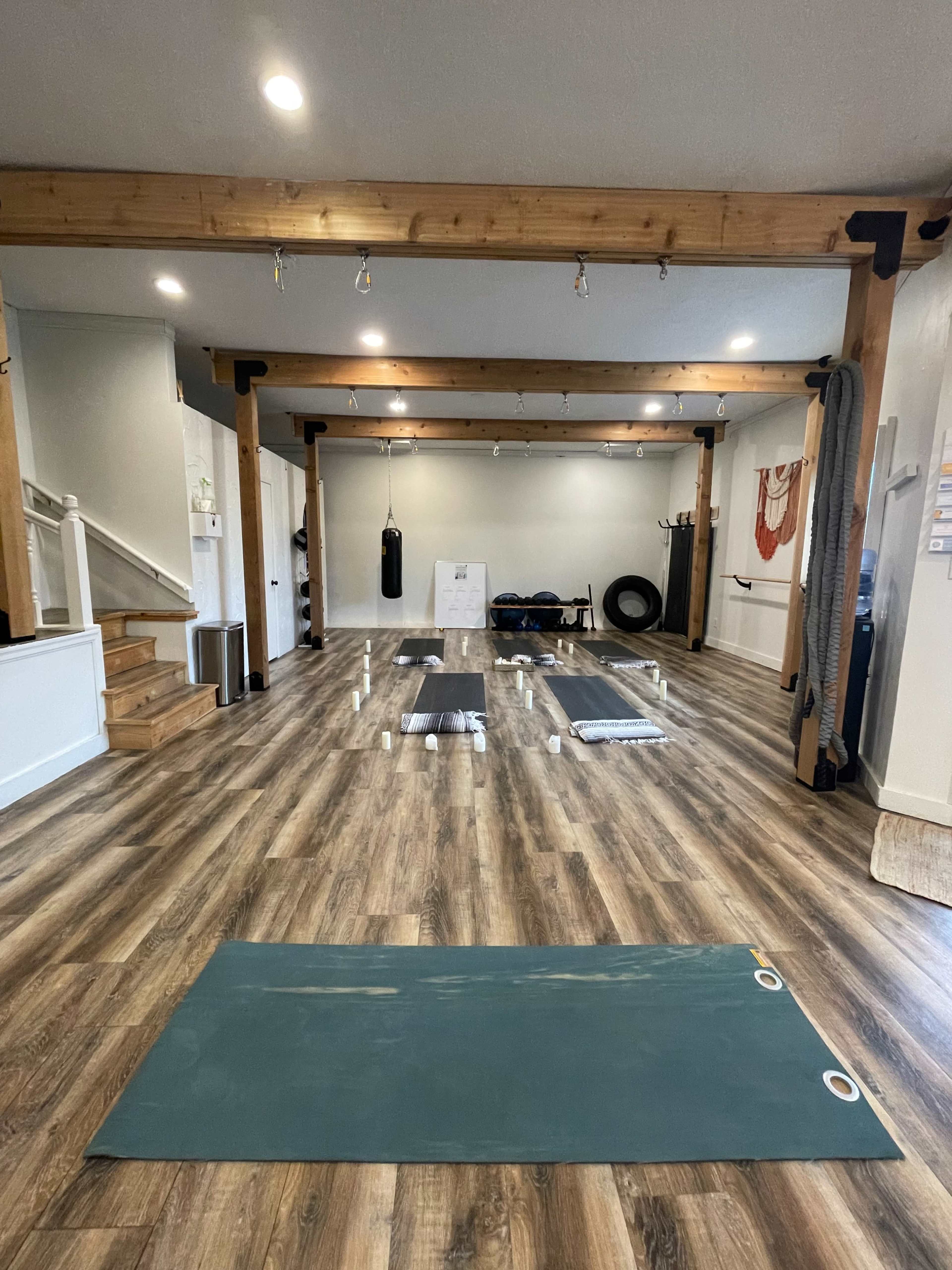The image shows an interior fitness studio with several exercise mats arranged on a wooden floor, along with workout equipment and various wall fixtures.