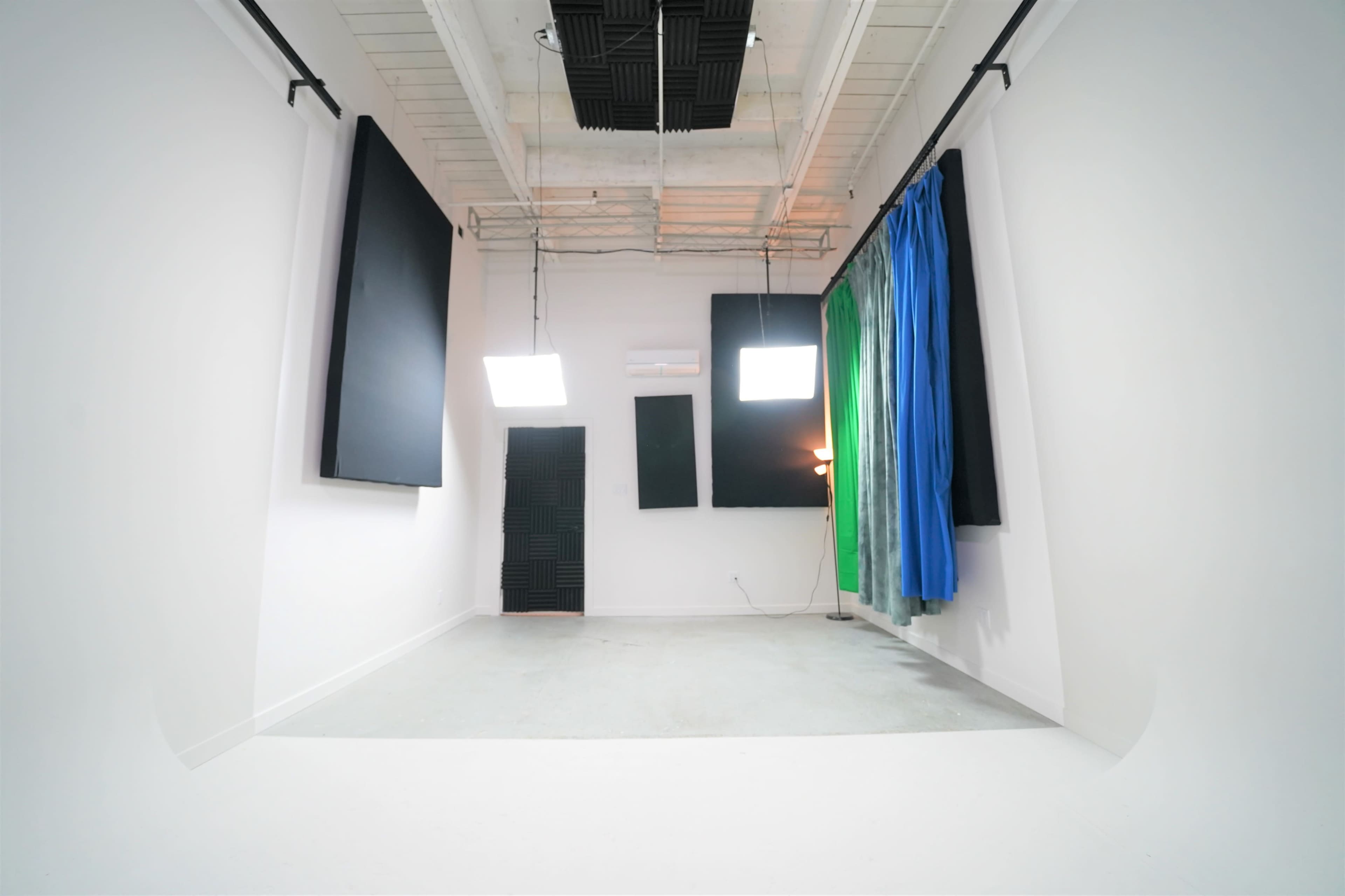 A minimalist studio space with large black panels on the walls, colorful fabric drapes hanging, and overhead lighting.