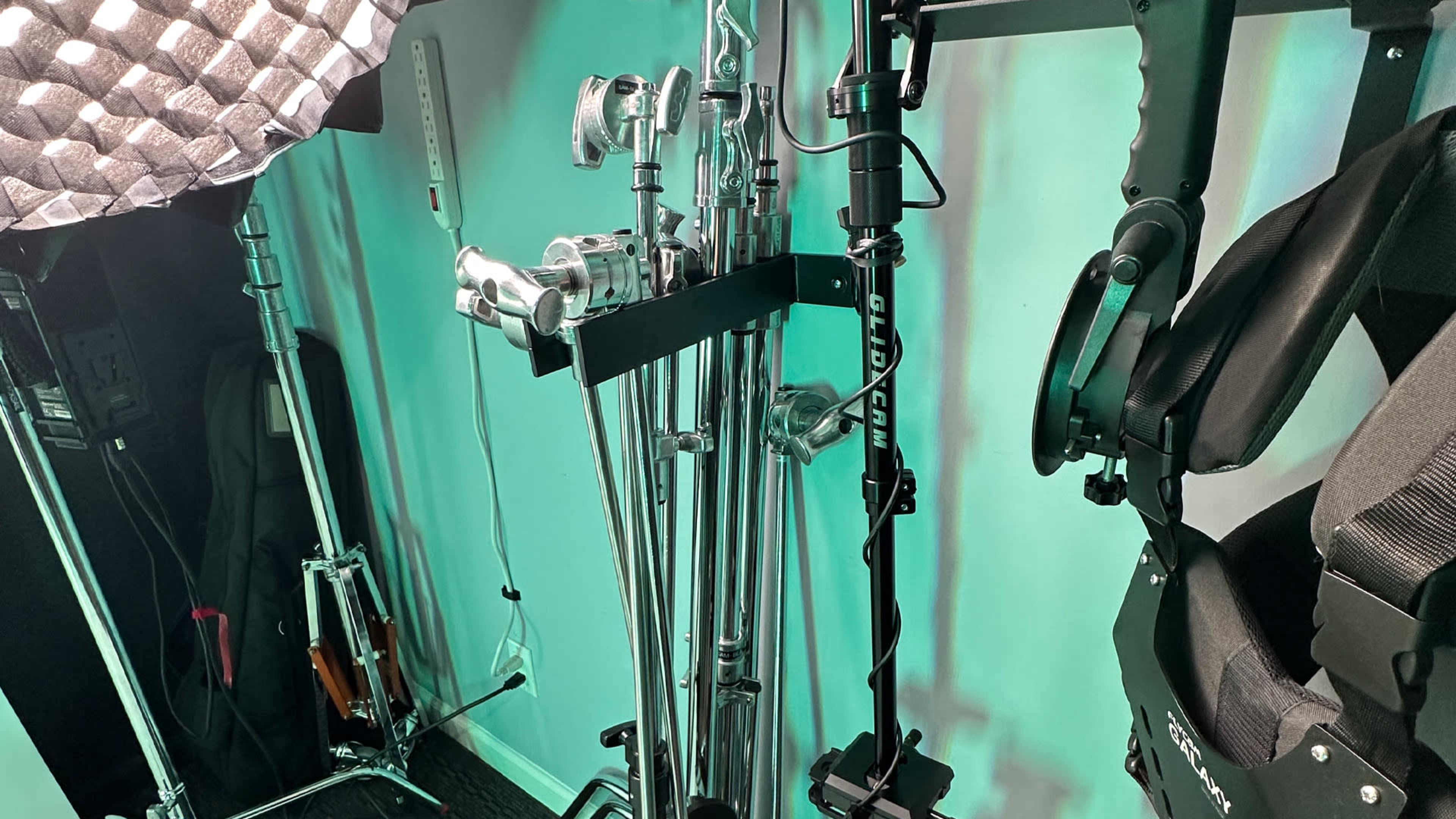 Various metal equipment stands arranged next to lighting gear and a black harness in a studio setting.