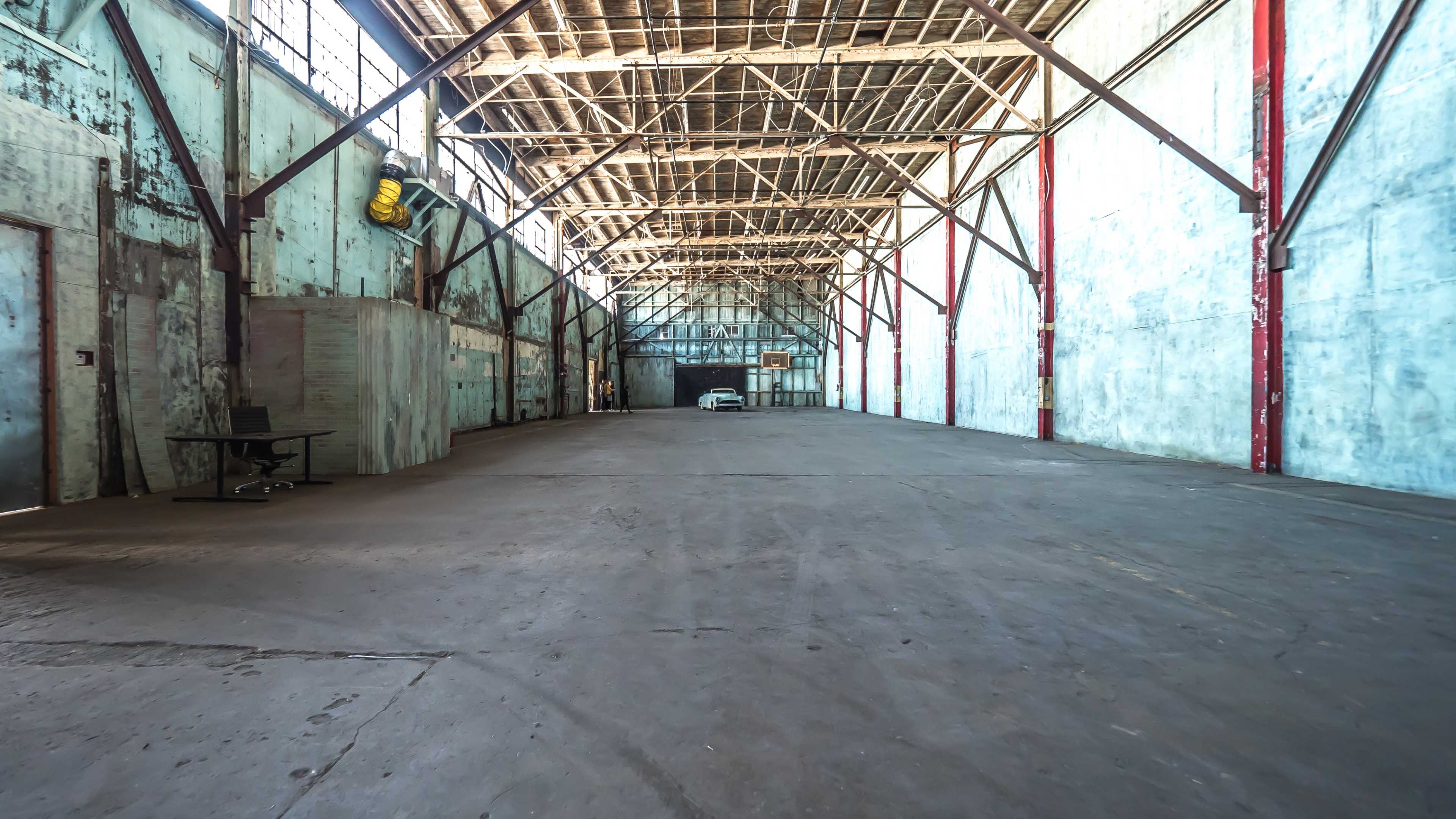 The image shows a spacious, empty warehouse with high ceilings and exposed wooden beams.