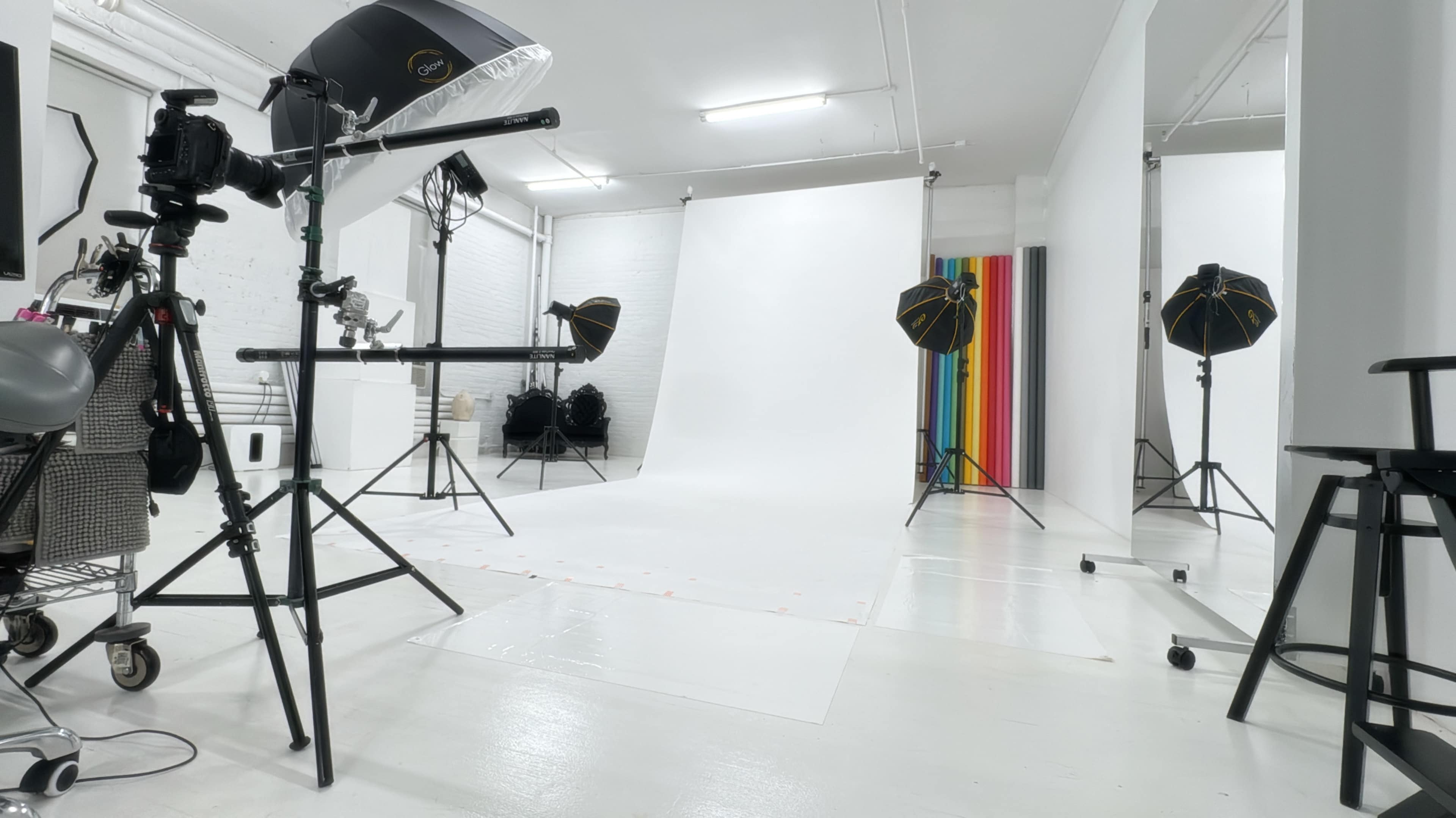 The image shows a photography studio with various lighting equipment, a white backdrop, and a colorful striped panel on one side.