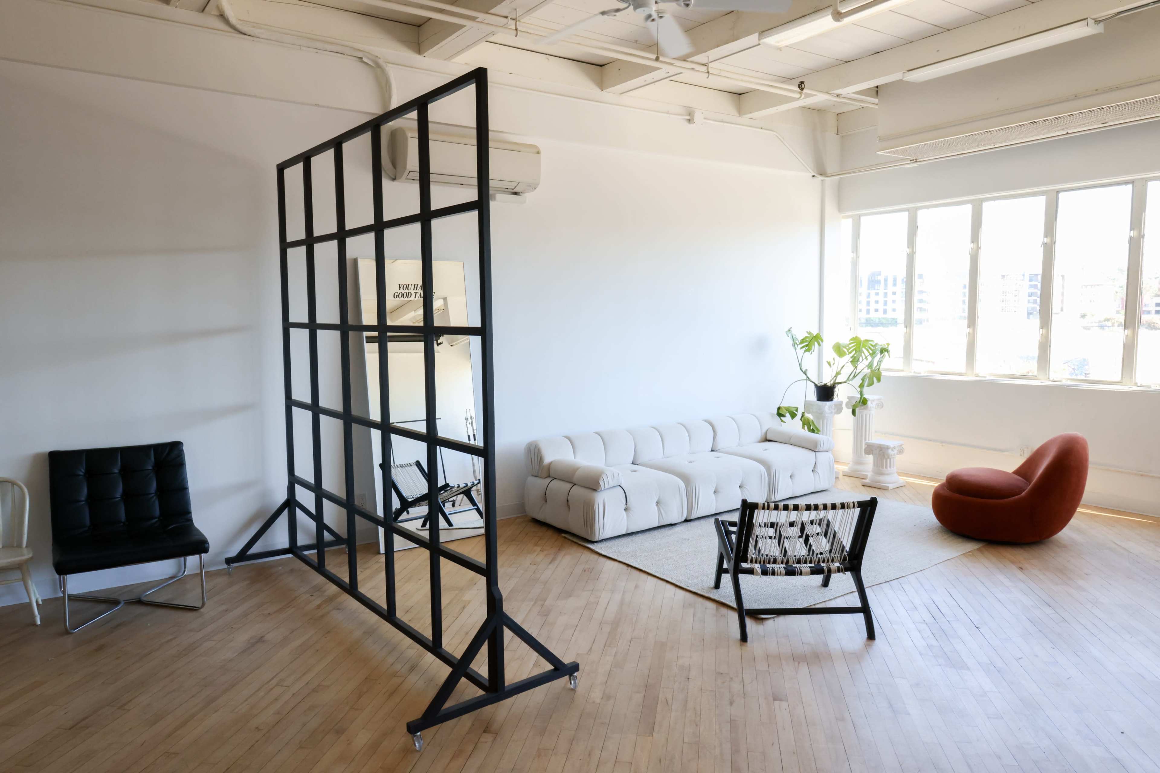 A spacious, well-lit room with modern furniture, including a white sofa, an orange chair, and a partition with a grid design.