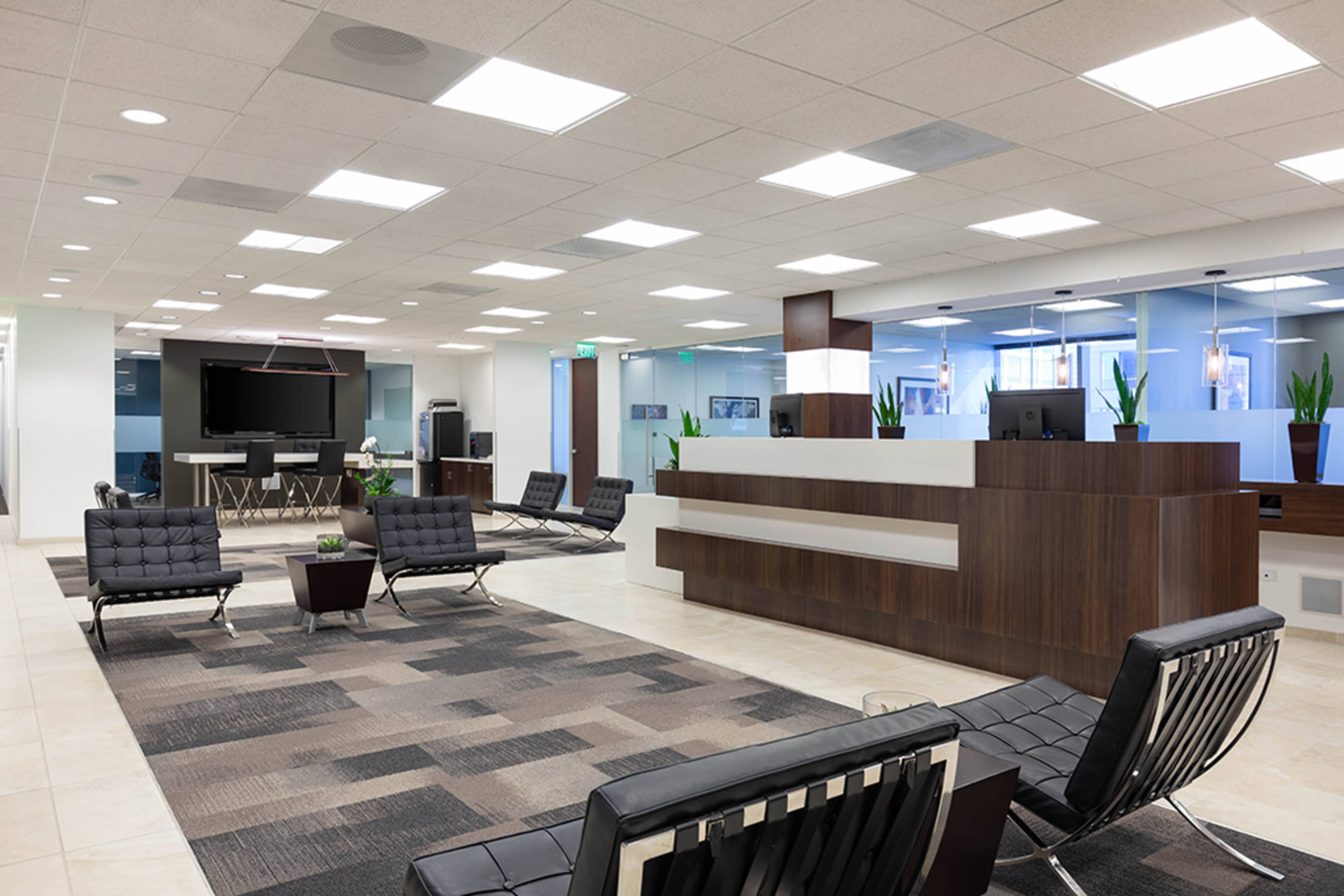 The image shows a modern office reception area with seating, a reception desk, and large windows.